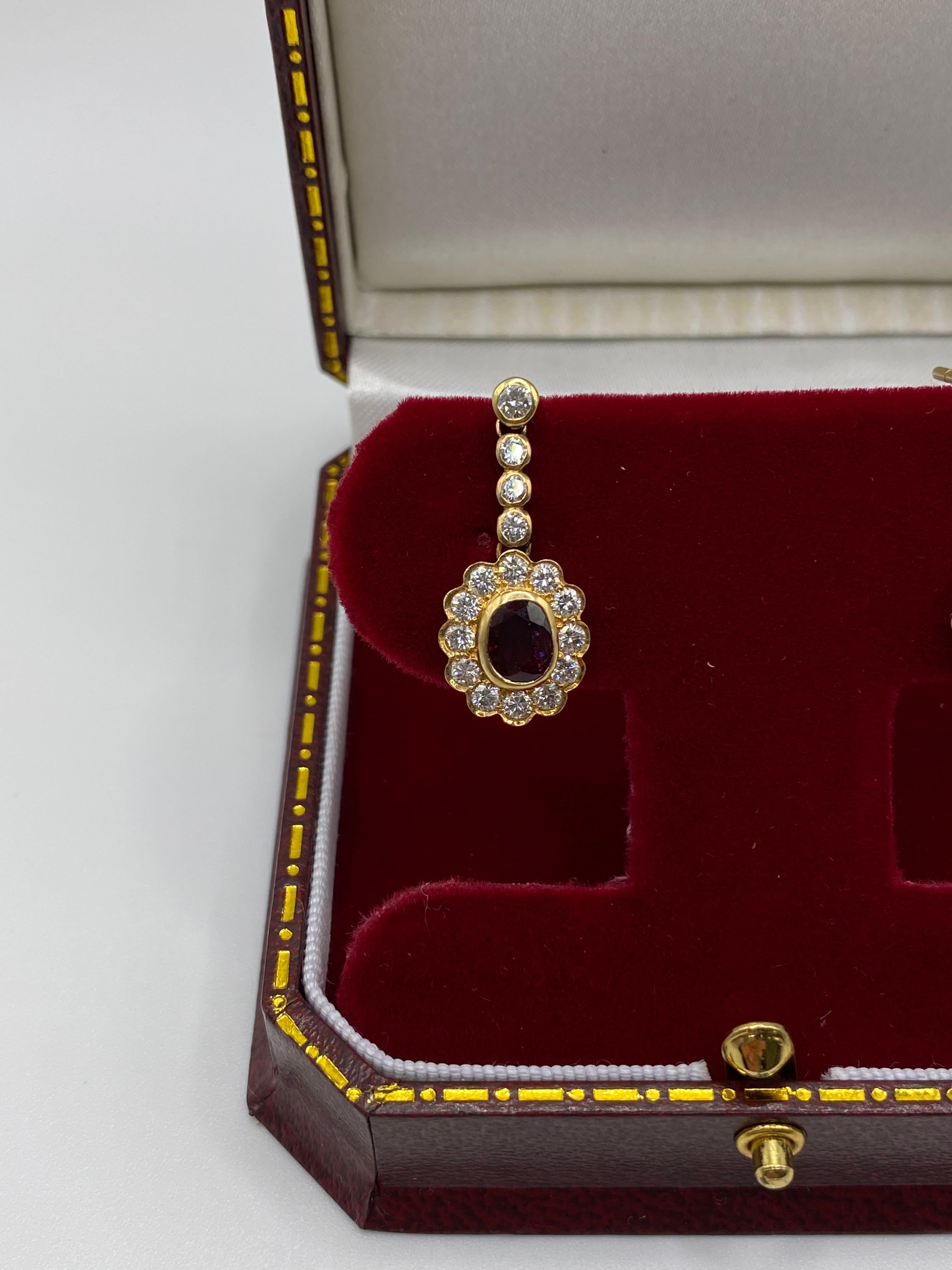 A pair of ruby and diamond pendant earrings, each supporting an oval cluster set with an oval ruby, measuring approximately 5.5 x 4.2 x 4, weighing approximately 0.81 carats, framed by brilliant-cut diamonds to a similarly set diamond line, British