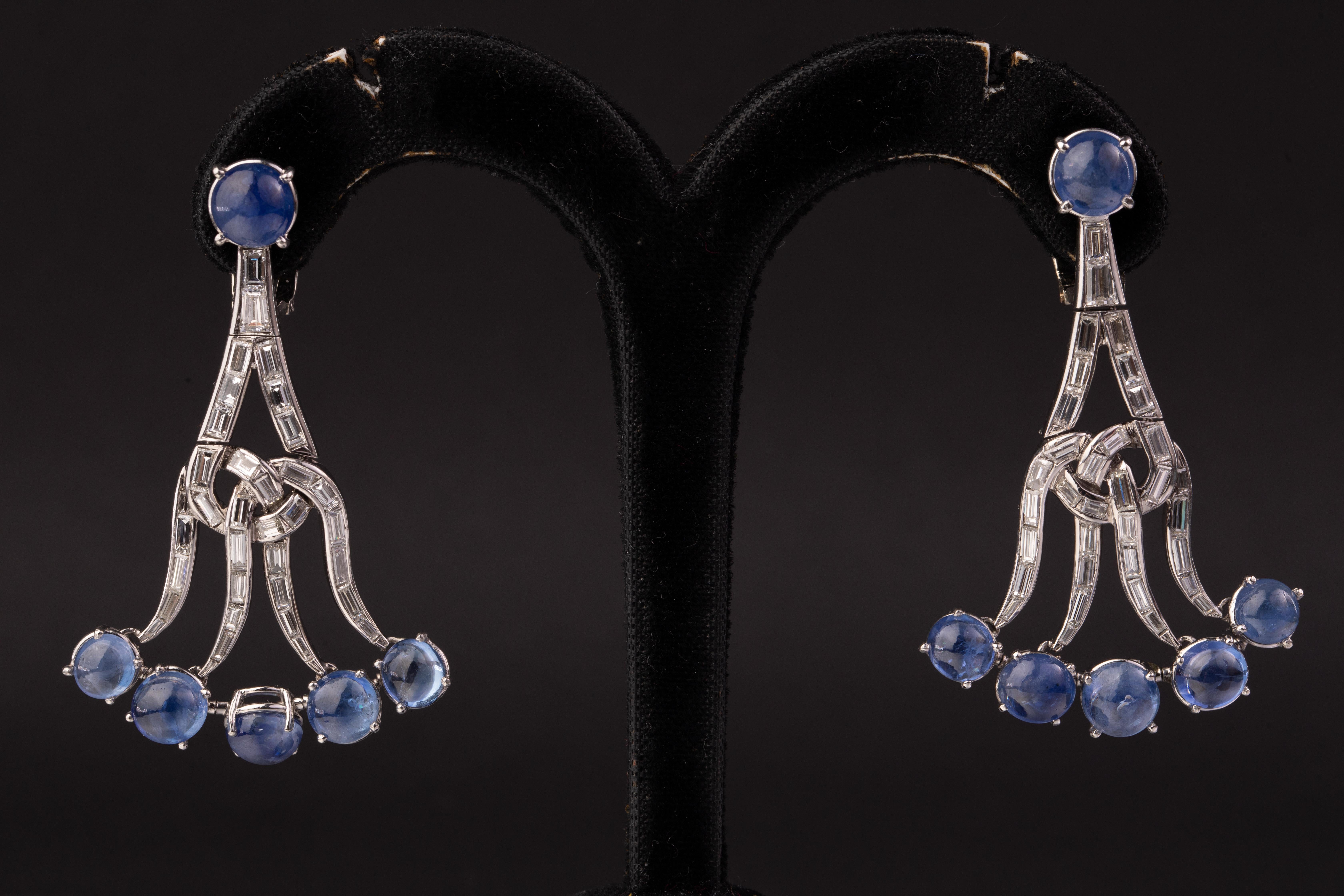 A Pair of Sapphire and Diamond Chandelier Ear-Pendants. Made in the USA, circa 1980.

Each designed as a stylized chandelier, suspending six cabochon sapphires of deep cornflower blue hue, together weighing approximately 16 carats, accented