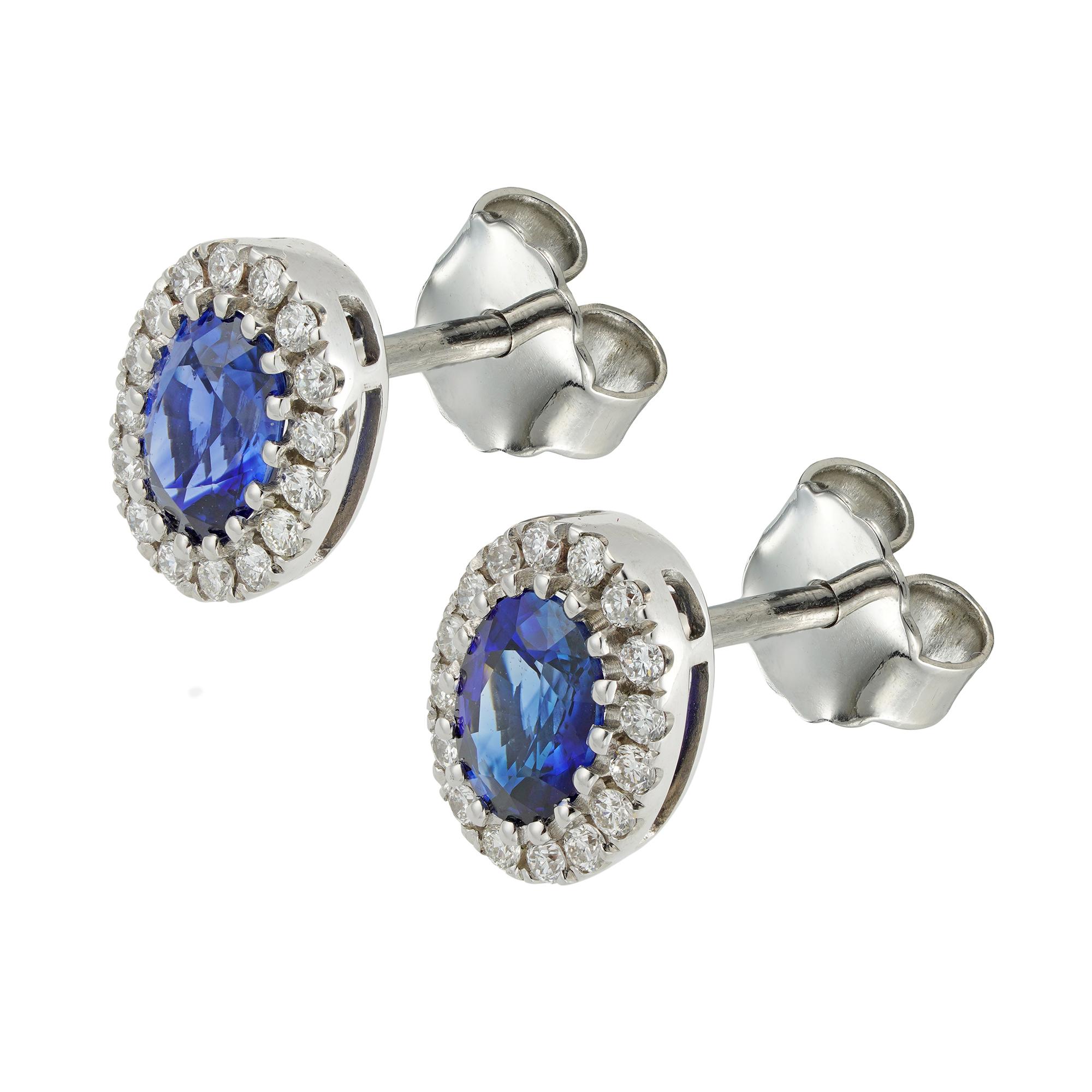 A pair of sapphire and diamond cluster earrings, each earring with an oval-cut sapphire weighing 1.48 carats the pair, surrounded by small brilliant-cut diamonds weighing 0.28 carats in total, all claw-set in white gold mount, with post and scroll
