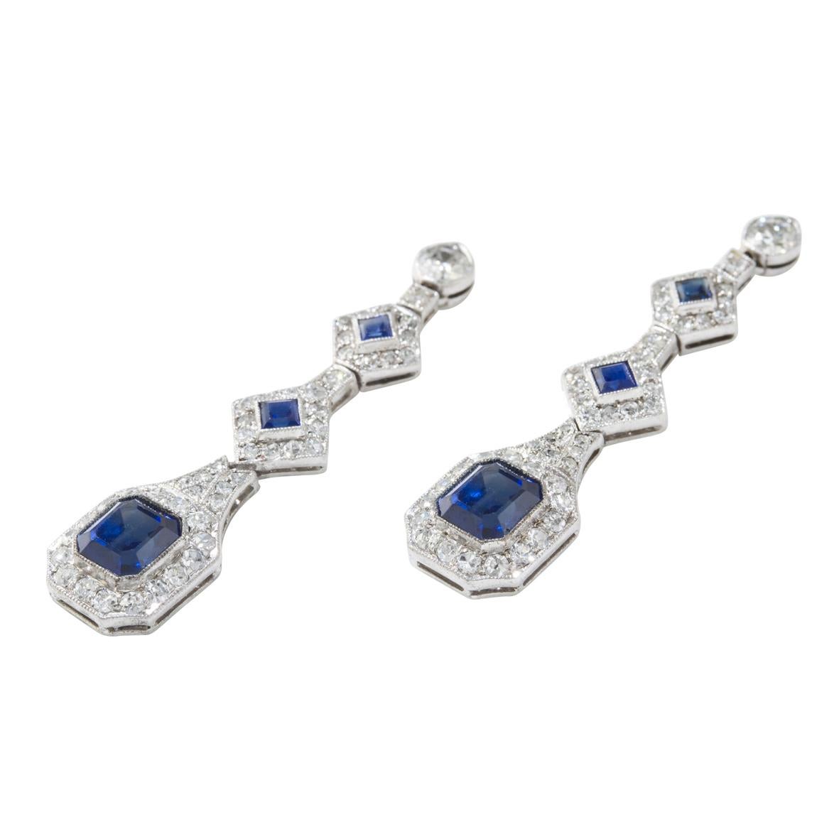A pair of sapphire and diamond drop earrings, each earring comprising of an emerald-cut sapphire, estimated to weigh a total of 2.5 carats, to the centre of an eight-cut diamond cluster surmounted by two further step-cut sapphires and diamond