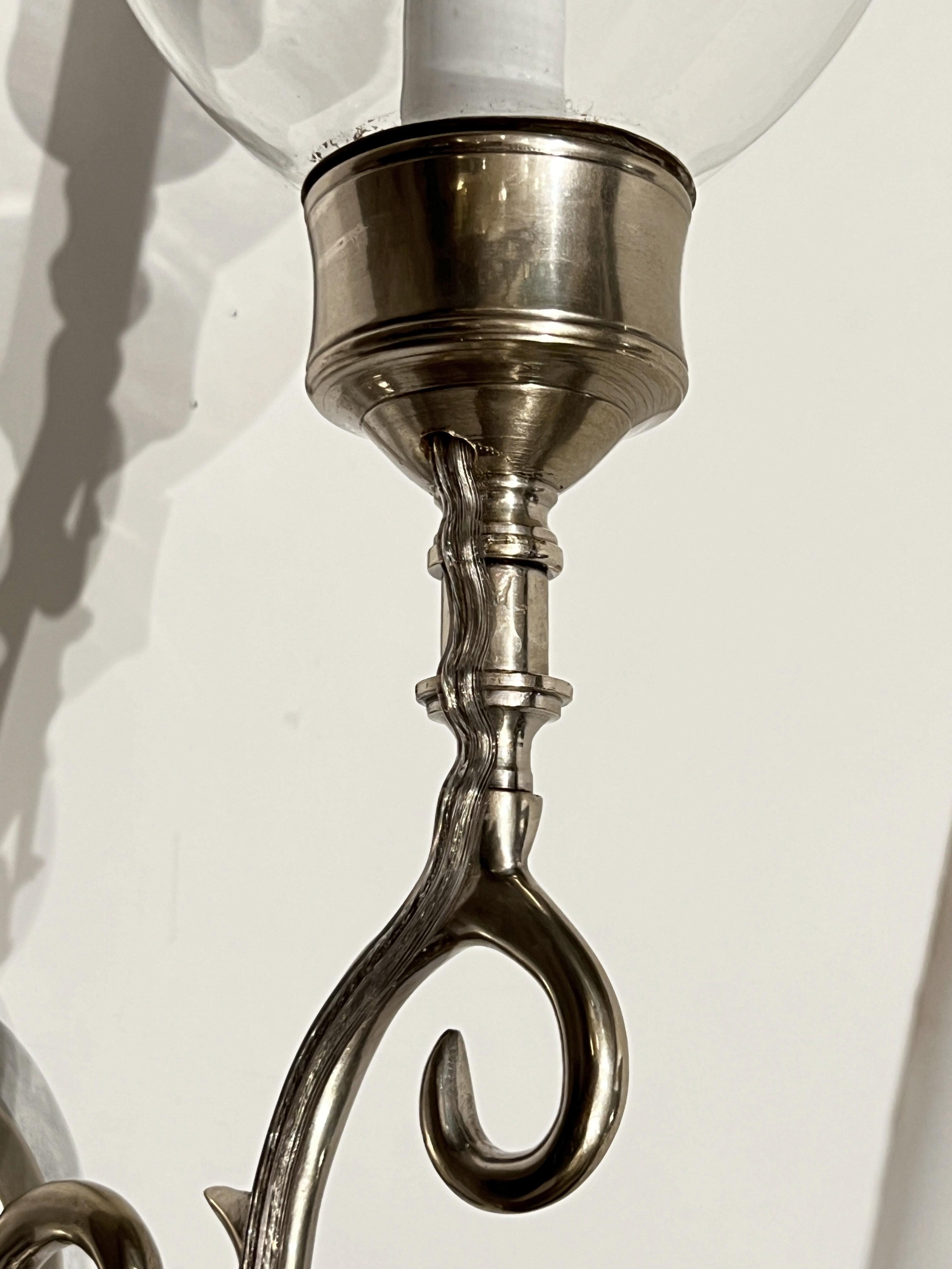Una coppia di appliques con piastre posteriori in mogano intagliate a mano con finitura bianca antica dipinta a mano. Ognuno di essi ha una presa a candelabro all'interno di un paralume trasparente a uragano, fissato con un braccio e una coppa