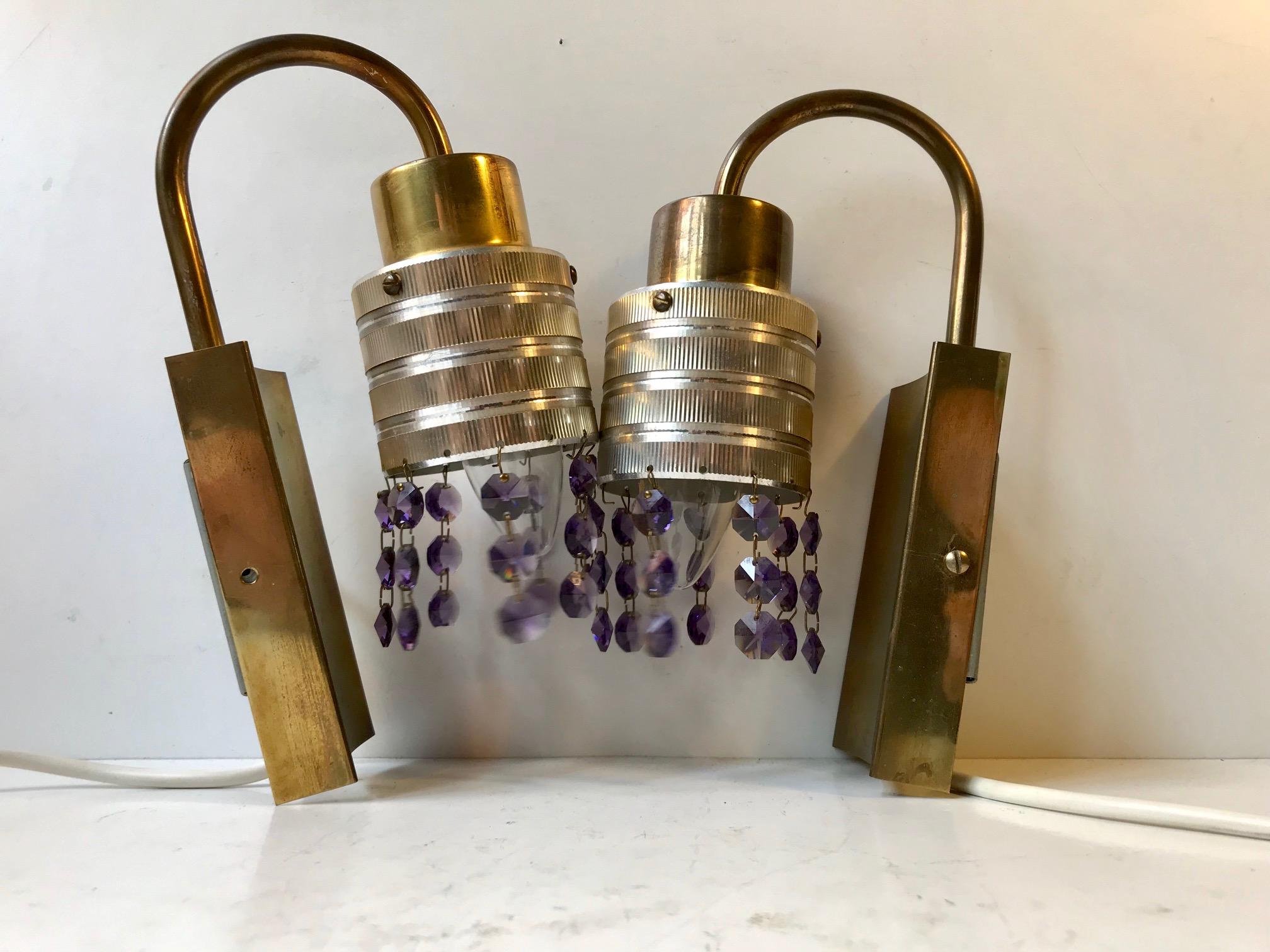 A pair of midcentury 'Swag' wall lamps of brass mounts and aluminium engine turned shades set with rows of purple and faceted crystal prisms. Anonymous maker/designer in the style of Hans Agne Jakobsson.