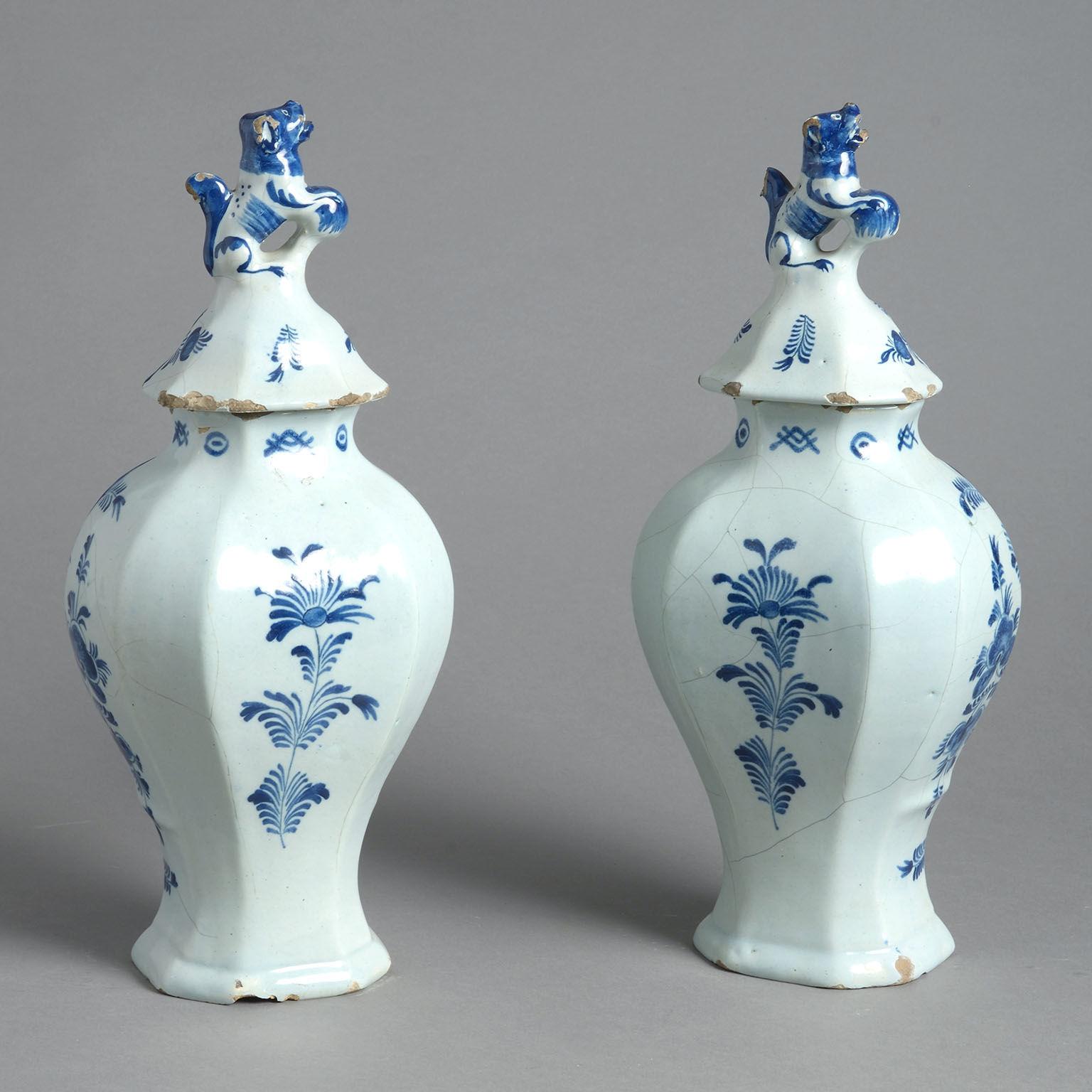 A pair of signed 18th century delft lidded vases, the baluster forms painted with roses within a molded Rococo cartouche in blue on a white ground. Surmounted by domed covers with dog finials. Signed by Johannes Harlees.