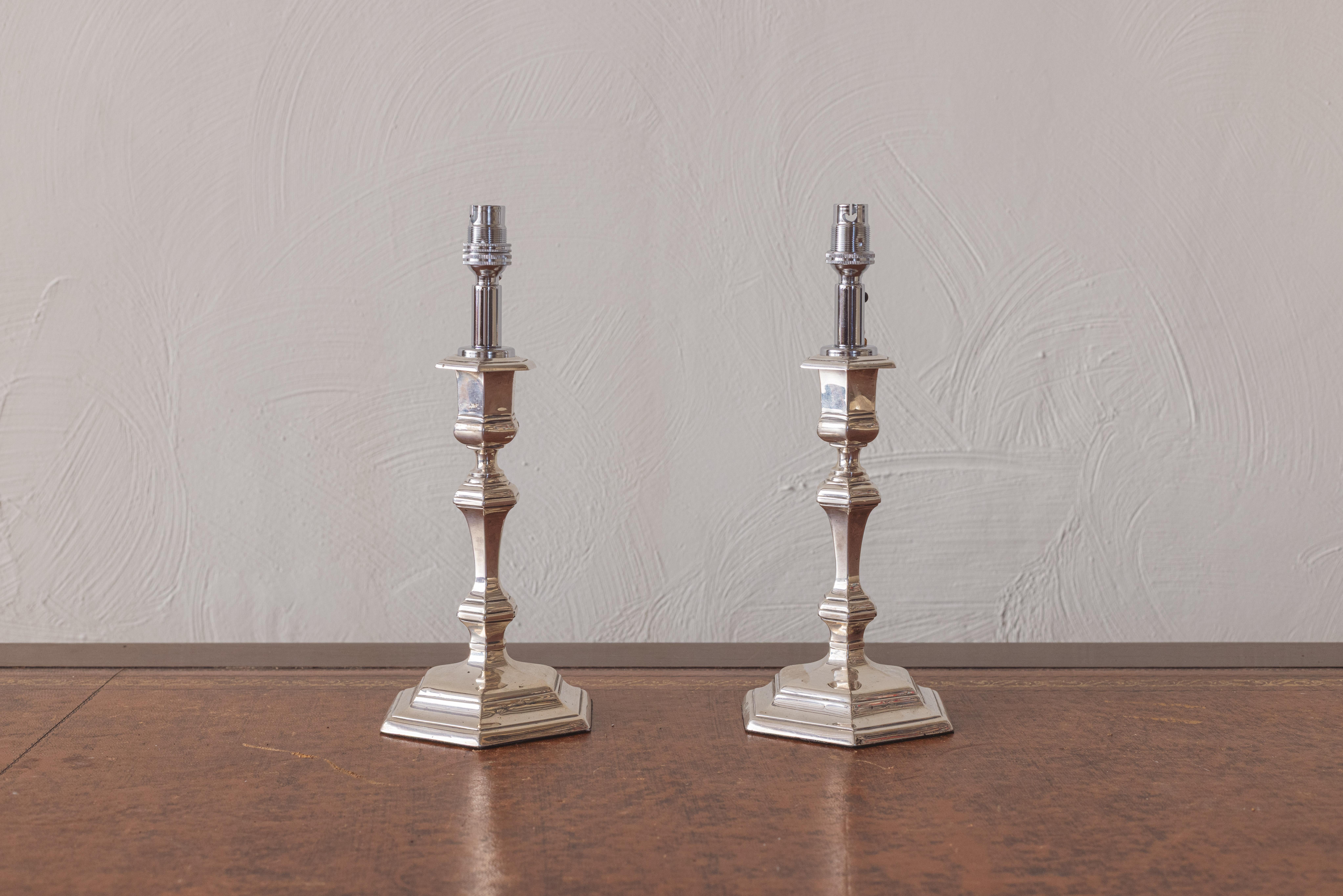 Un par de pequeños candelabros de plata de Eduardo VII, de Goldsmiths and Silversmith Co. Ltd. Cada una en estilo George I, sobre base hexagonal con tallo balaustre. Recientemente iluminada, con un flexo trenzado marrón y una toma de enchufe del
