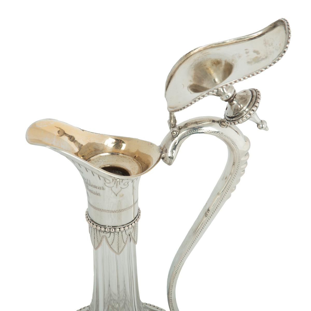 A pair of silver-mounted crystal Royal presentation claret jugs, each with a globular diamond cut body and long facetted neck, applied with silver spouts with hinged lids and arched handles engraved alternately ‘To E. Hobbs from Henry and Waldemar,