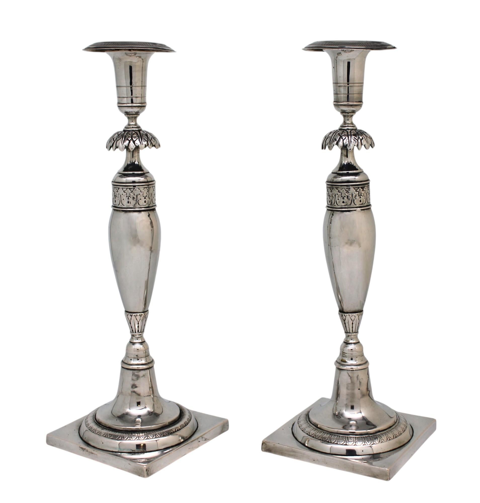Este exquisito par de candelabros de plata para Shabbat muestra el refinado arte de los plateros alemanes de principios del siglo XIX. Cada candelabro está elegantemente montado sobre una base cuadrada, elevada por una plataforma circular adornada