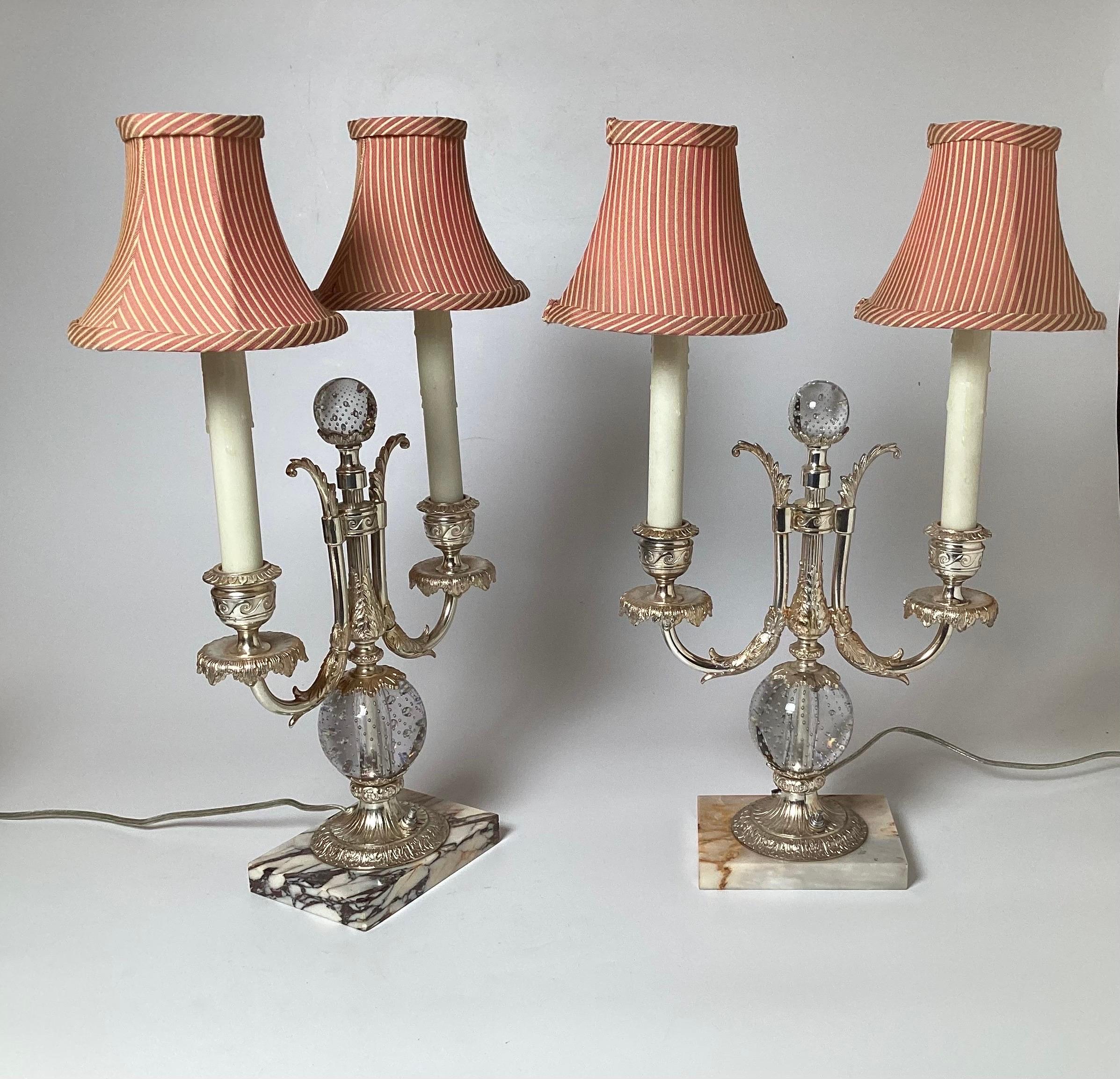An elegant pair of silvered bronze and glass candelabra lamps by Pairpoint . The two light lamps with silvered bronze mounts with glass sphere at the center and top with control bubbles in the glass. The base is a white and grey marble. Recent