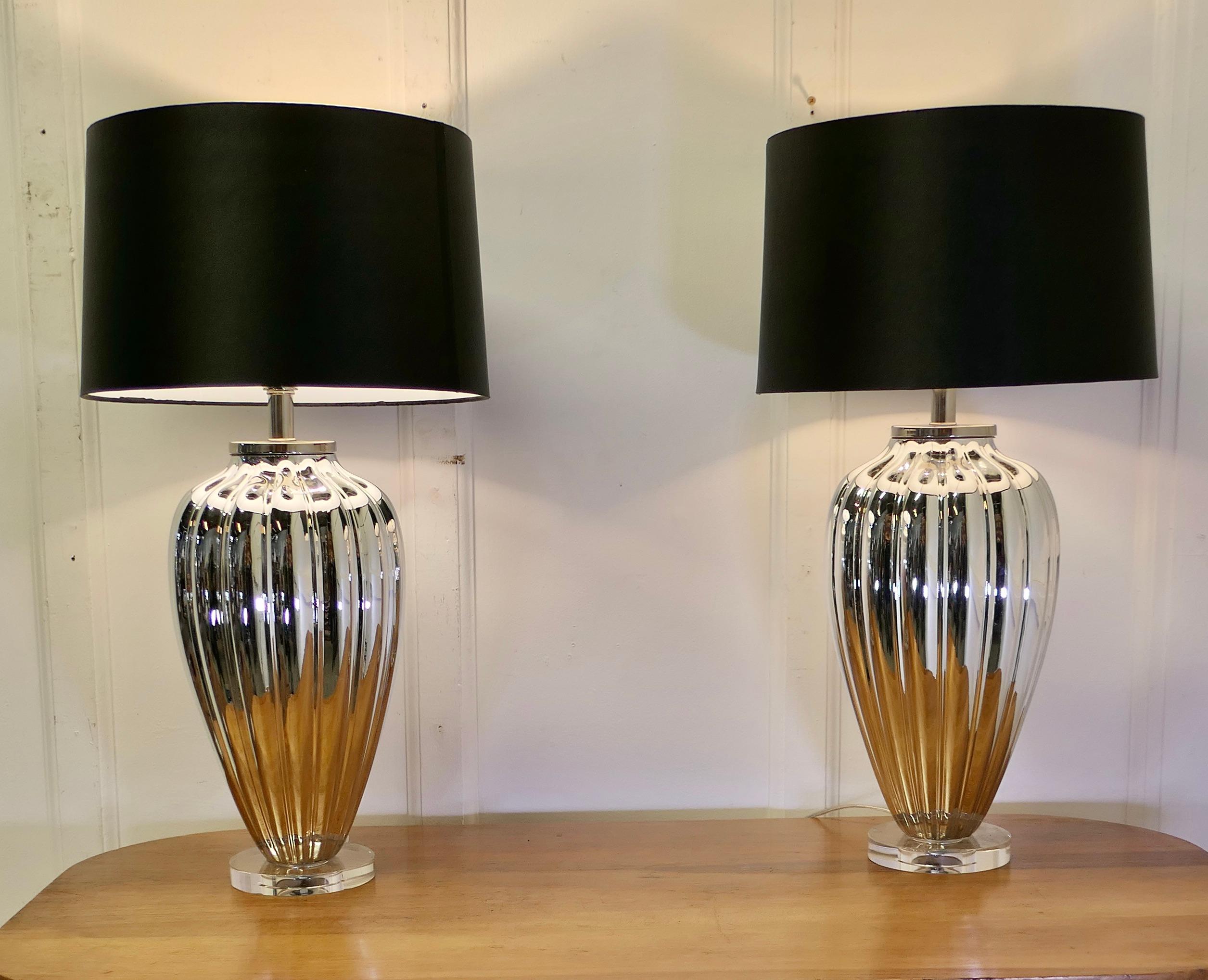 A Pair of Silvered Glass Table Lamps 

The lamps stand on a circular glass foot, they have a large fluted glass baluster which is silvered  

These are a stunning pair lamps and are matched with new black linen shades  
The lamps are in good