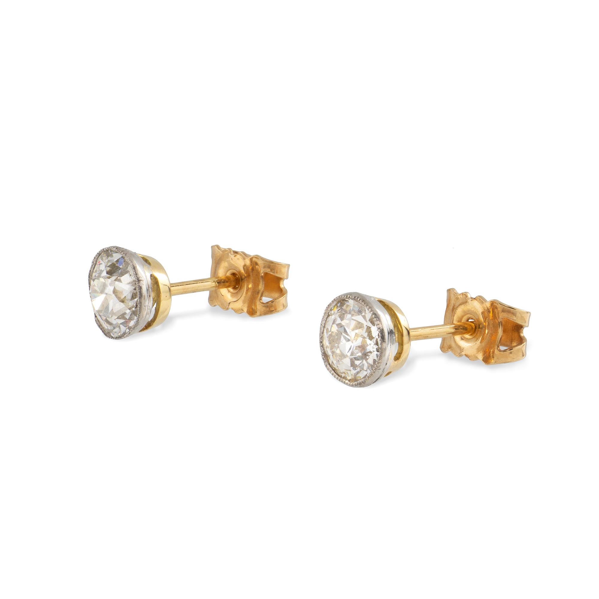 A pair of single stone diamond stud earrings, the round old cut diamonds with estimated combined weight 1.70 carats, each rub-over millegrain-set in platinum with gold back, circa 1930, with later gold peg and C-scroll fitting, measuring