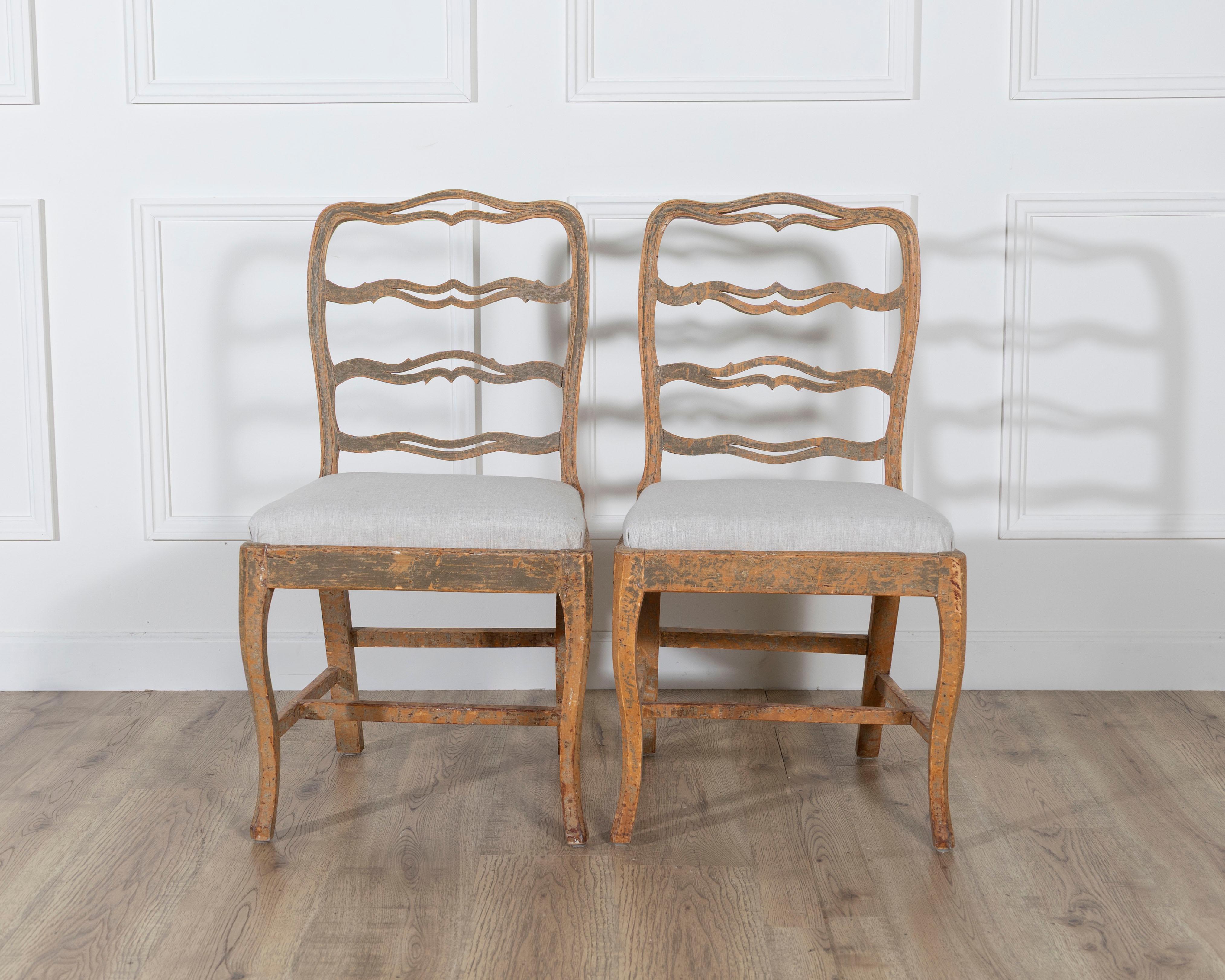 A charming pair of slender Gustavian chairs, Sweden, circa 1780. The gently curved ladder-backs feature the distinctive “smiling” details typical of the period, lending an inviting and graceful presence. Expertly scraped to reveal traces of their