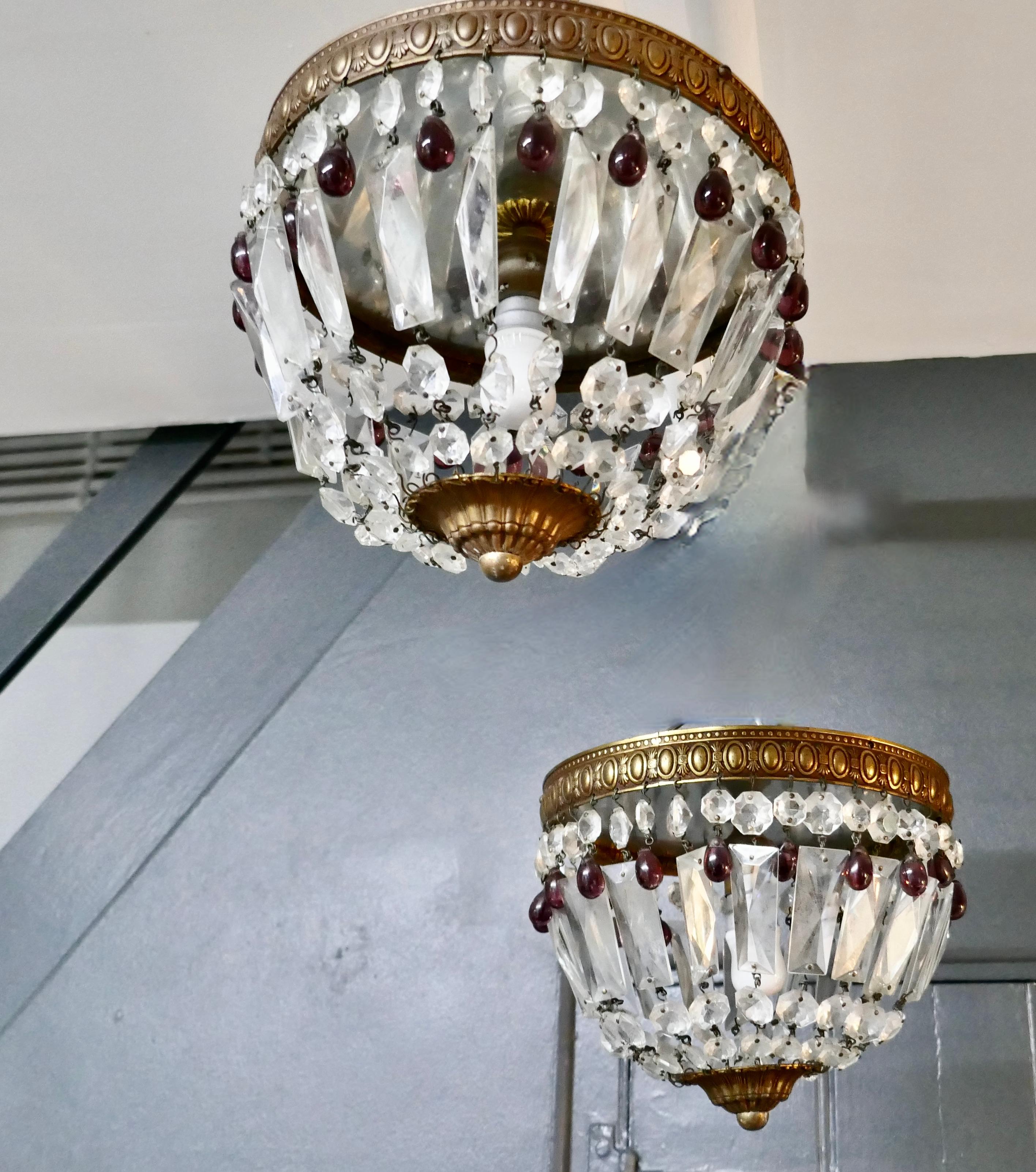 A pair of small French Empire style crystal basket chandeliers

This is a lovely pair they have an aged brass frame hung with crystal chains forming a basket and alternate garnet crystal drops between 
The chandeliers are in good and working