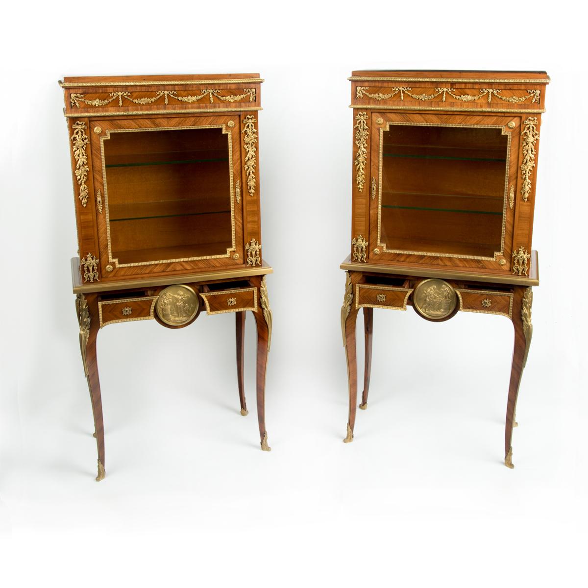 Una coppia di piccole vetrine in legno di re Napoleone III su cavalletti, ciascuna di forma rettangolare con un singolo armadio vetrato posto su una base con due cassetti a fregio mascherato che fiancheggiano un grande tondo classico in ormù