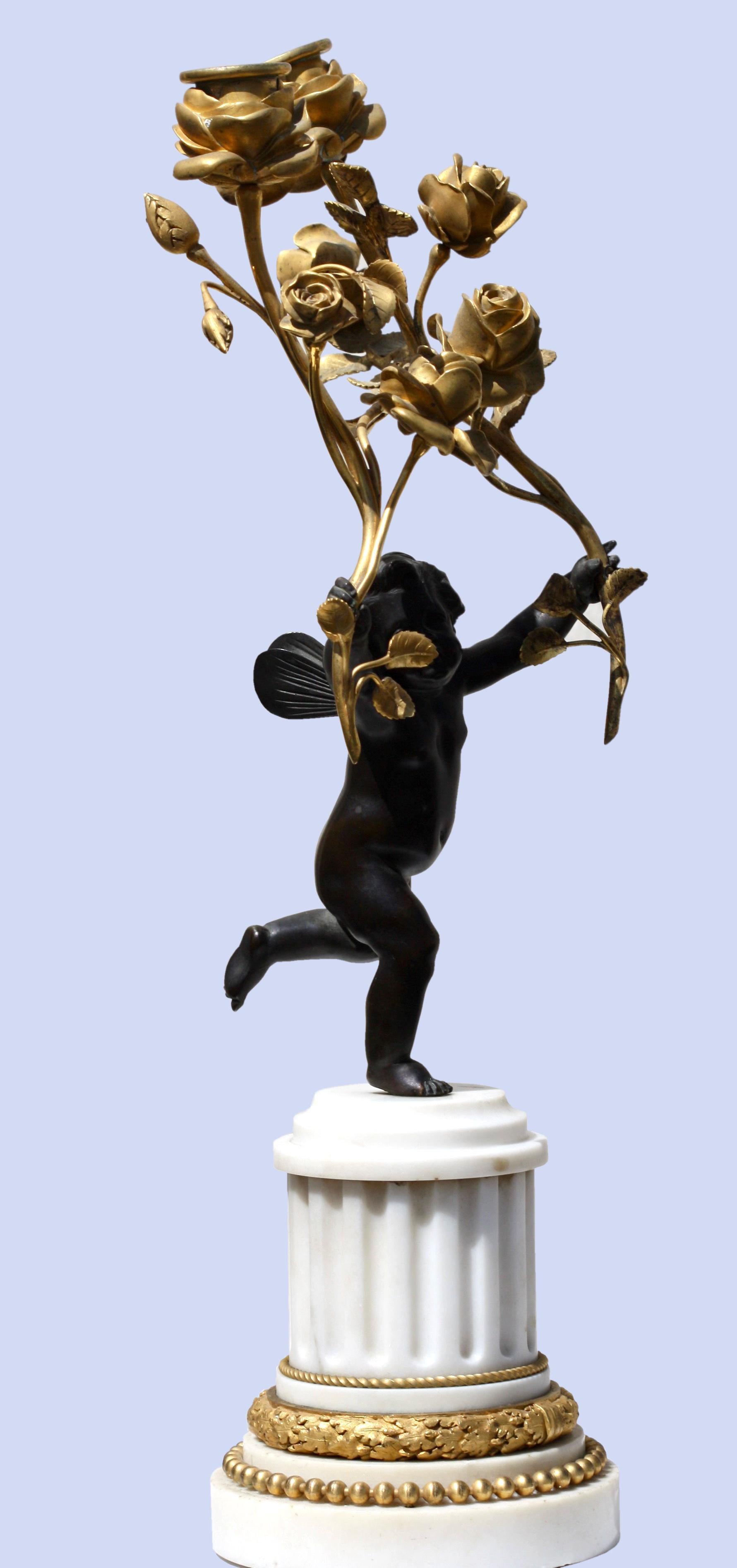 A pair of standing cherub patinated bronze and gilt-bronze figural candelabrum,
after Jean-Baptiste Pigalle
in the form of a cherub supporting two scroll branches, on a white marble columnar base, 
Measures: Height 17.25, (43.81 cm.), width 9