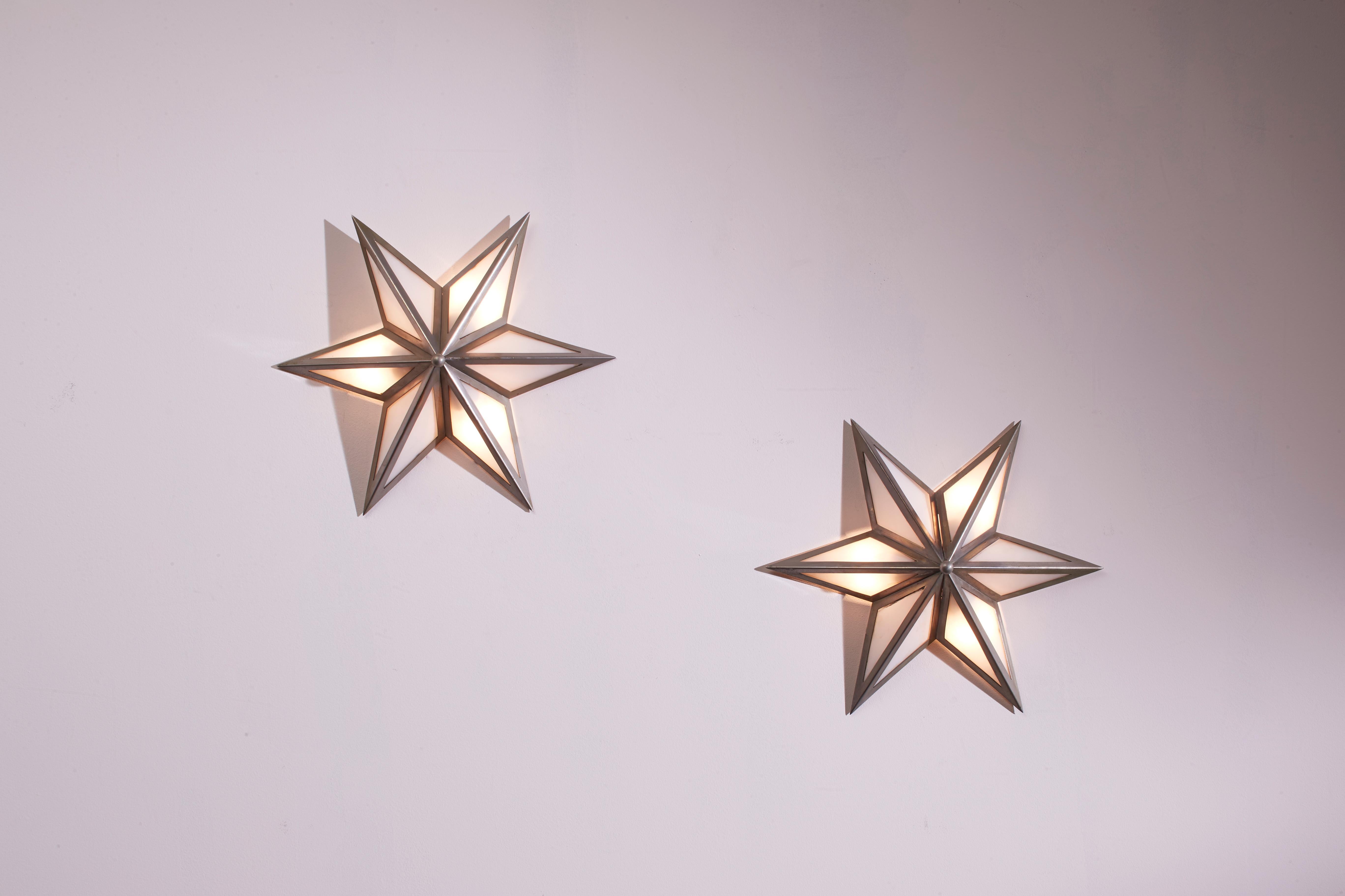A pair of star-shaped wall sconces, made of steel and glass, represents an authentic example of Italian craftsmanship from the Sixties.

Thin metal profiles frame an opal glass diffuser, shaping a luminous star. This set of wall lamps, two in brass