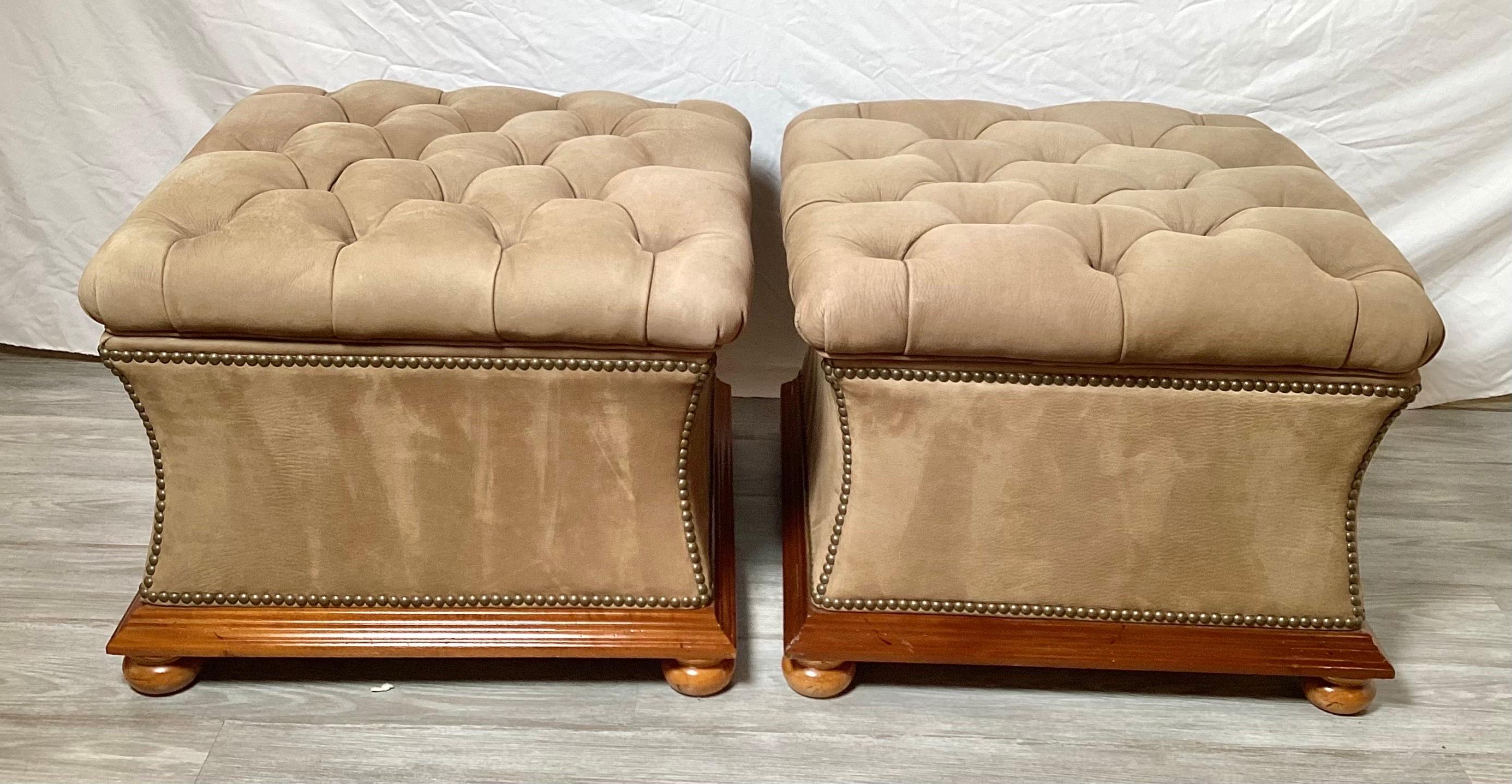 A chic pair of square tufted storage ottomans. The matt finished leather with antiqued brass nail-head trim. The lids remove to reveal storage.