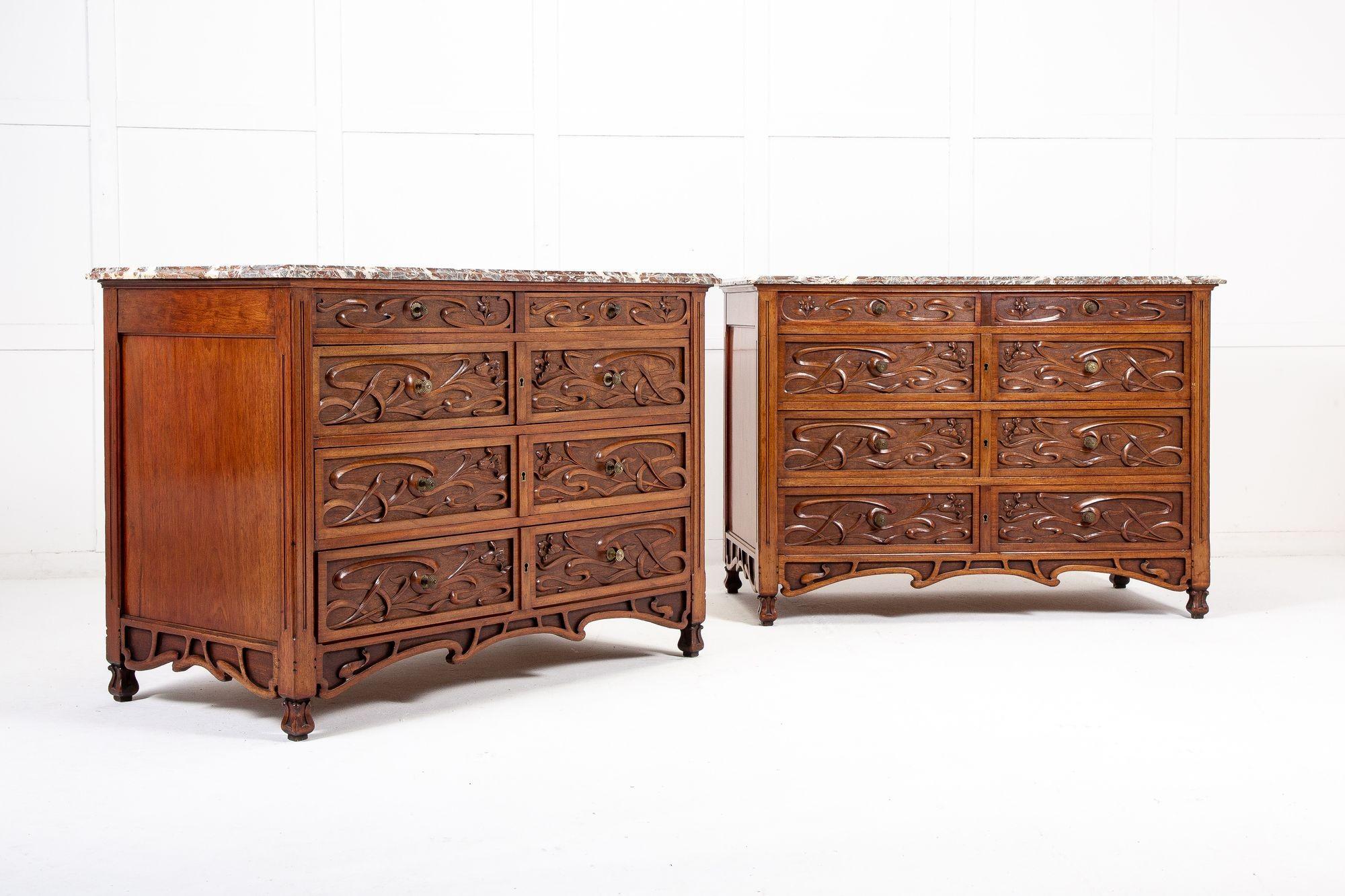 A pair of superbly carved Bruxelles chests of good scale and color, with original marble tops, having five drawers (two narrow upper drawers and three larger drawers below) and featuring flowing reed and flower fin-de-siecle carvings to drawer