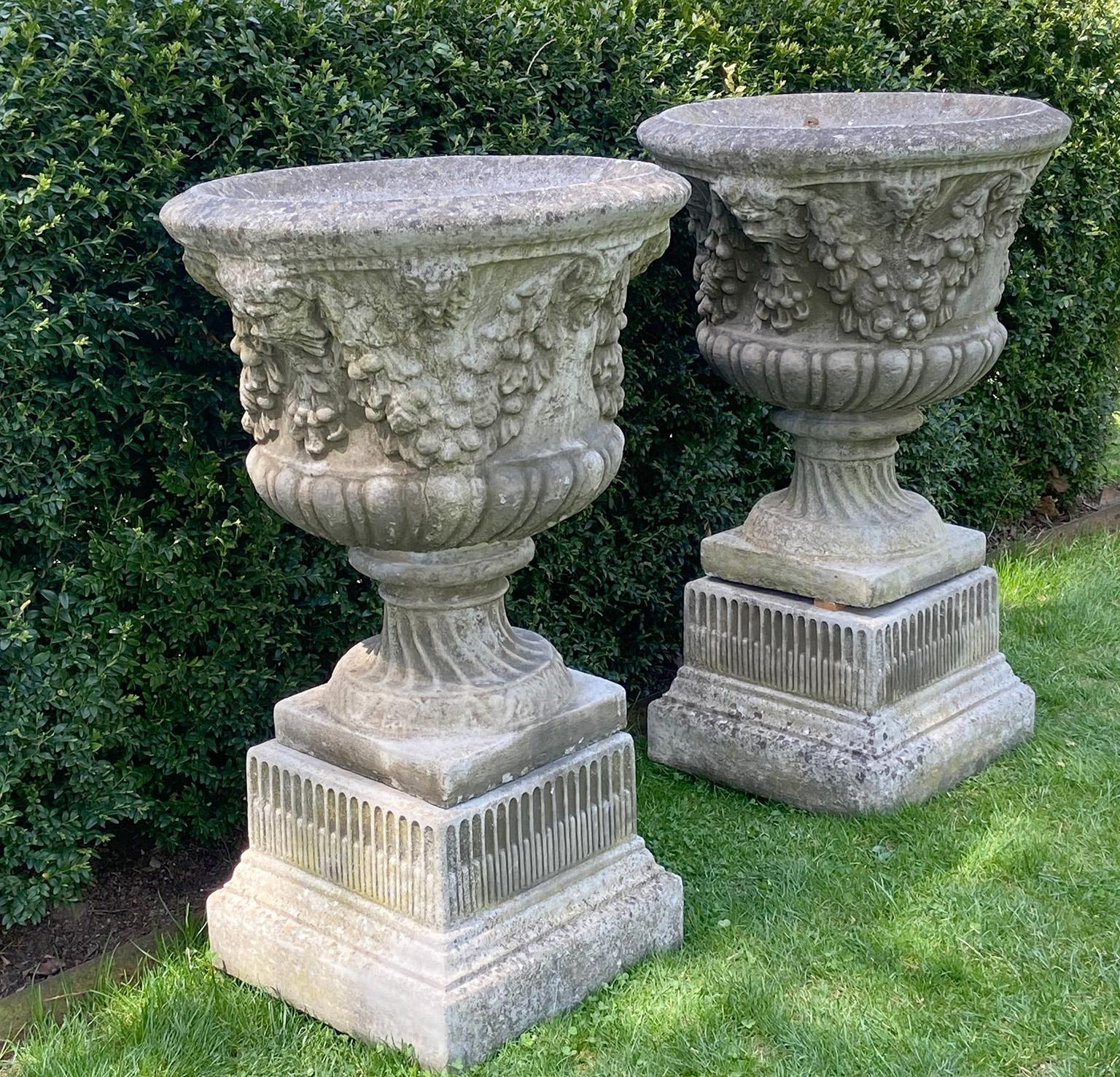 English Pair of Swag and Mask Composition Stone Urns on Decorative Pedestals