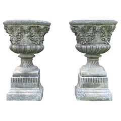 Paire d'urnes en pierre de composition en forme de guirlande et de masque sur piédestal décoratif