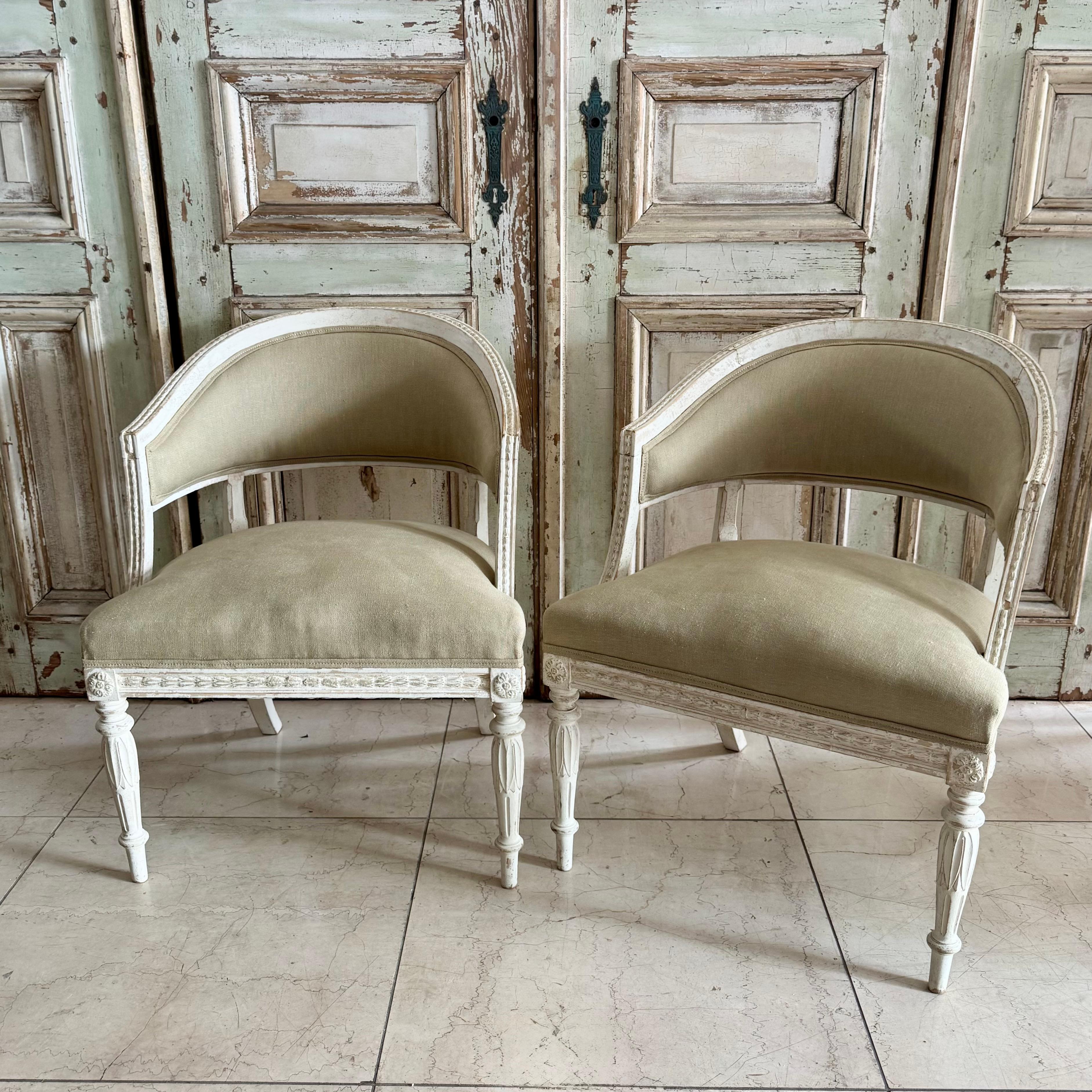 Coppia di sedie con schienale a botte Swediish del XIX secolo, verniciate in bianco e panna  e rivestito in lino neutro. Forma arrotondata, dettagliati intagli di fiori di campana sul poggiamano e gambe anteriori affusolate e intagliate con fiori di