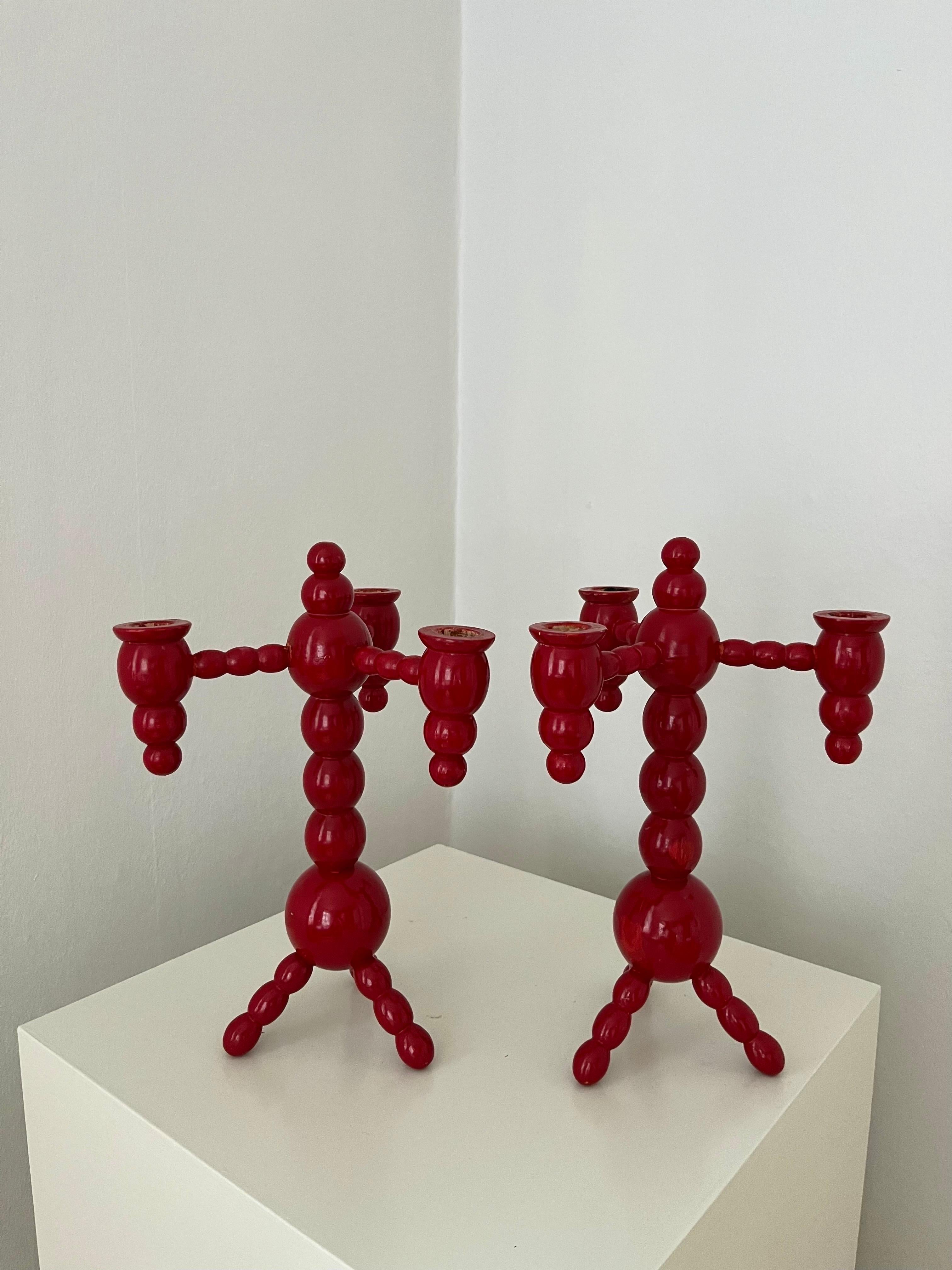 A pair of Swedish Christmas candelabras red painted wood bobbin 1970s. Each candelabra has 3 arms with a candle holder. Glossy red, bobbin style, 3 legs.
One of them signed with initials and '75 (for made in 1975). 
One with burn marks from candles