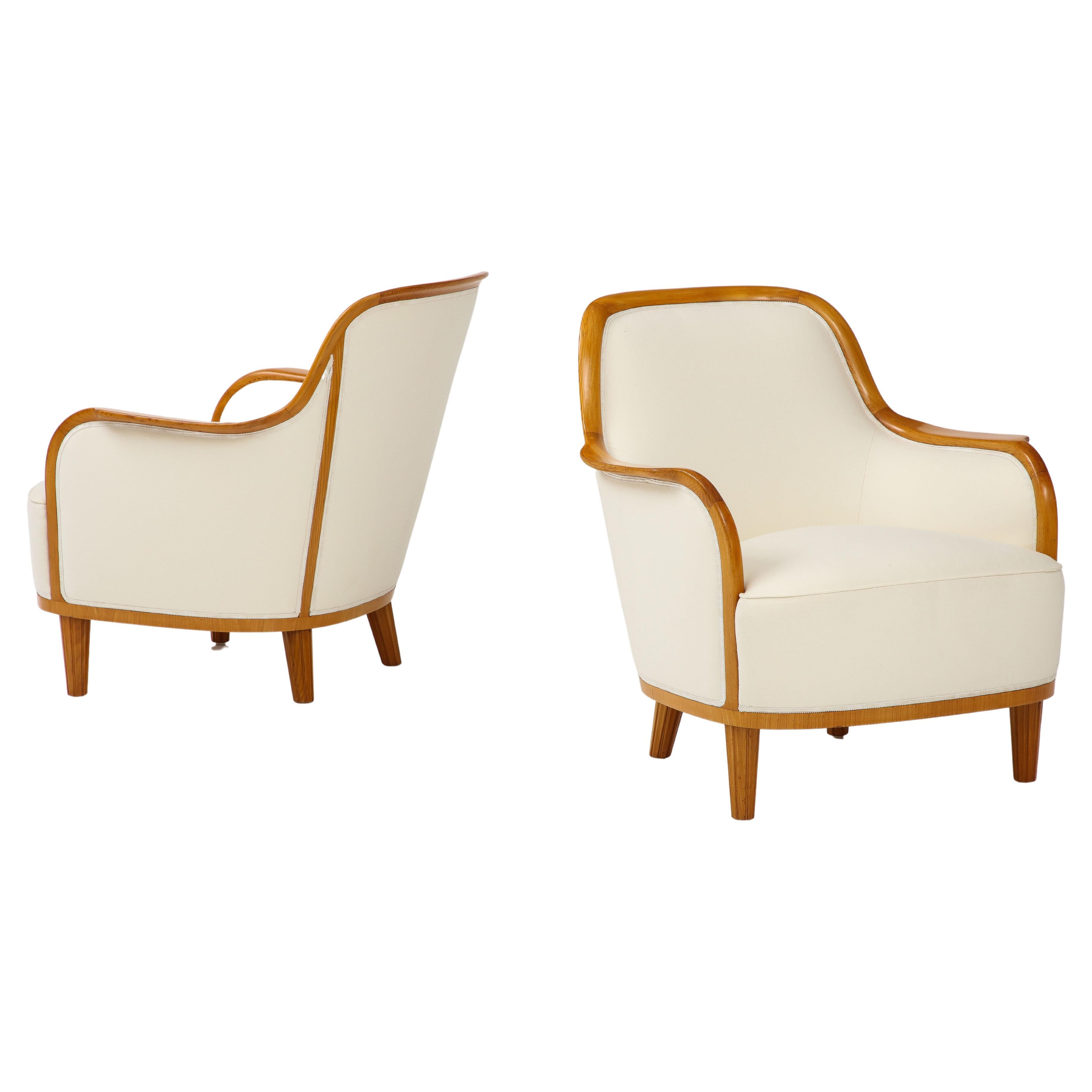 A pair of Swedish Grace elmwood and upholstered armchairs, produced by SMF Svenska Möbelfabriken Bodafors, with a generous curved back, downswept armrest, upholstered seat raised on circular fluted legs. New off white wool upholstery.