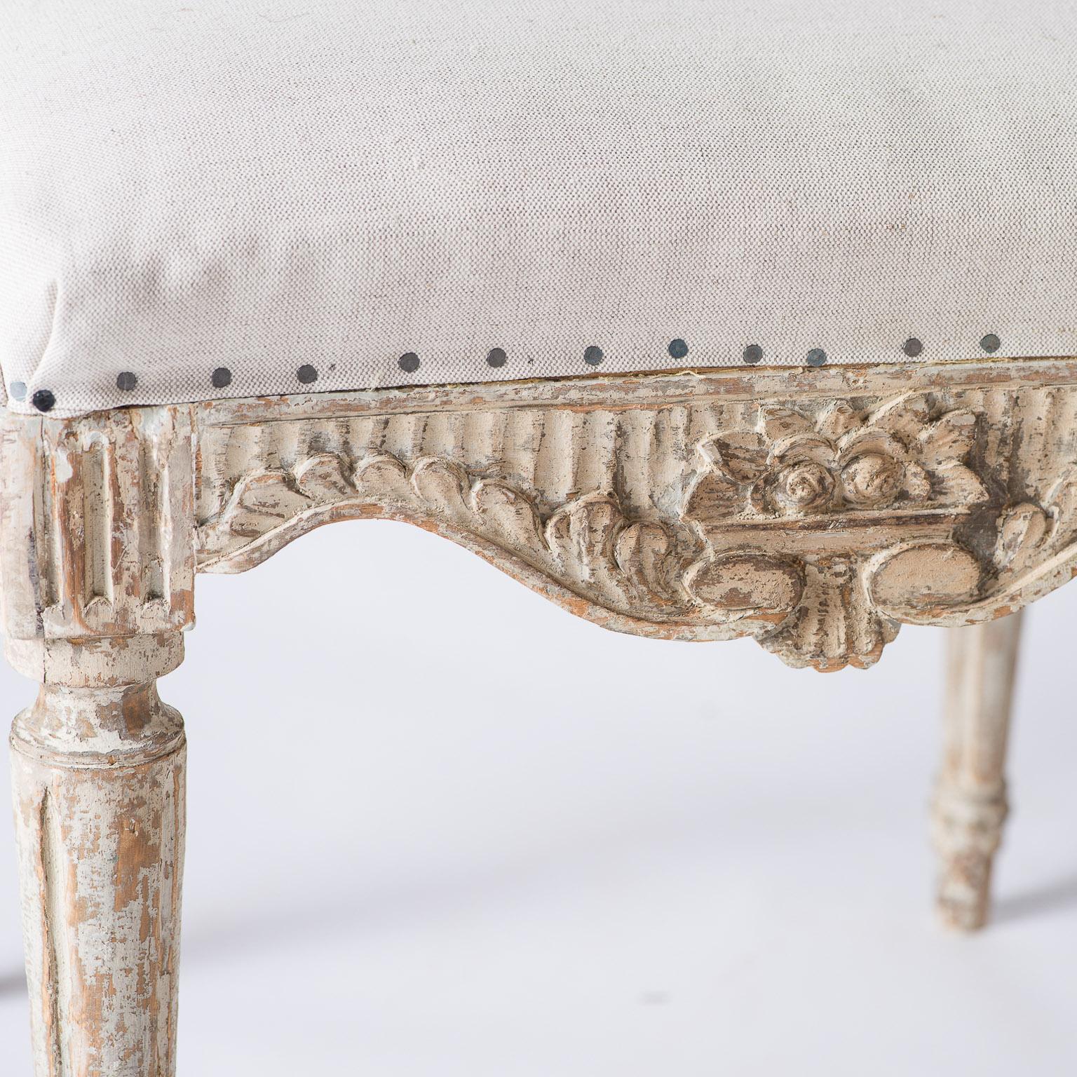 These footstools of the Gustavian period are unusual due to their generous size and elaborate carvings. They are finished on all four sides with a richly carved flower motif flanked by scrolls in the form of leaves and ending in elegant reeded legs.