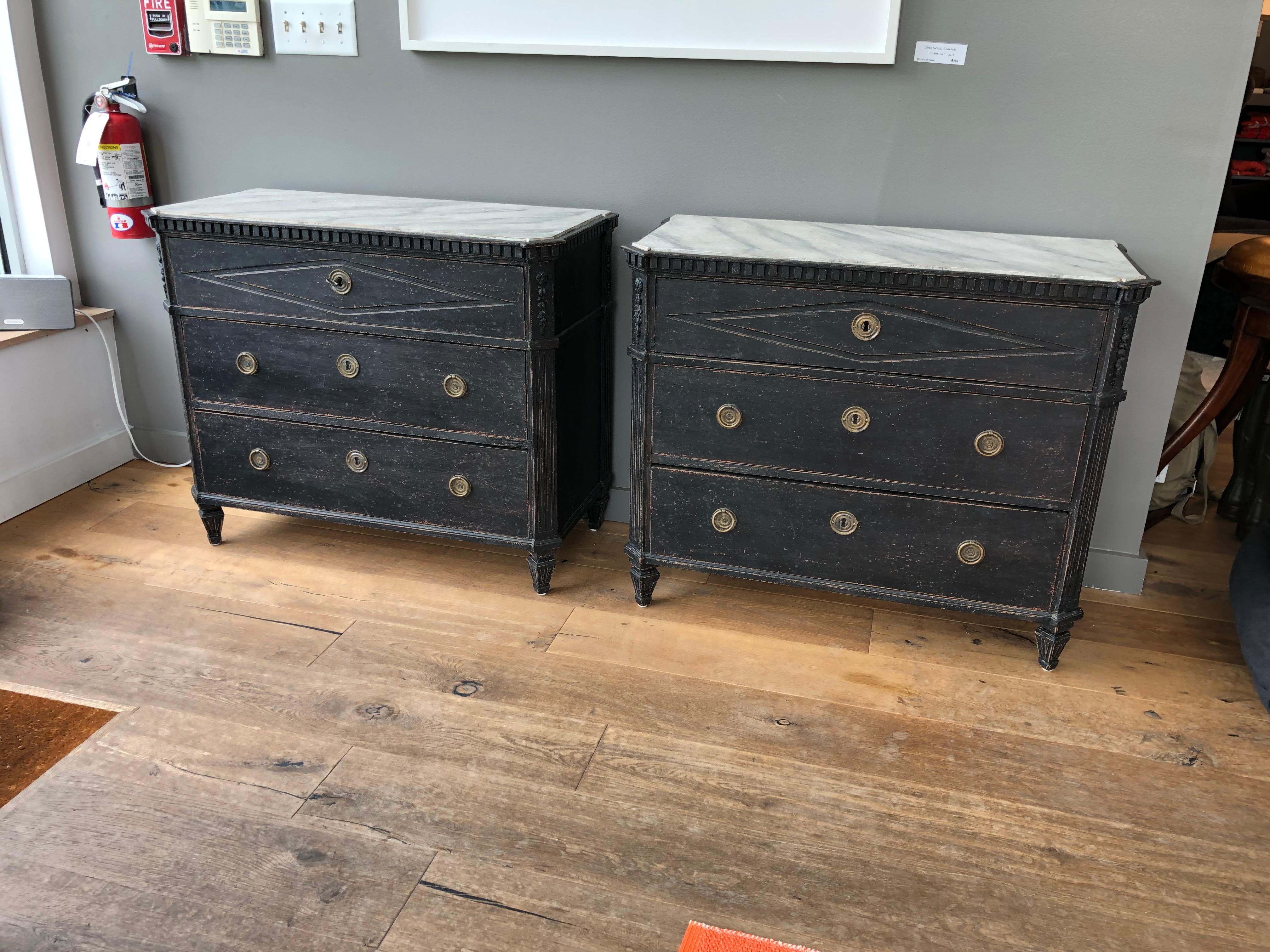 A pair of Swedish Late Gustavian style painted commodes, circa 1900, each with a rectangular top painted to simulate marble, the canted and fluted for corners above a dentil molding frieze and three long drawers, raised on square tapered and fluted
