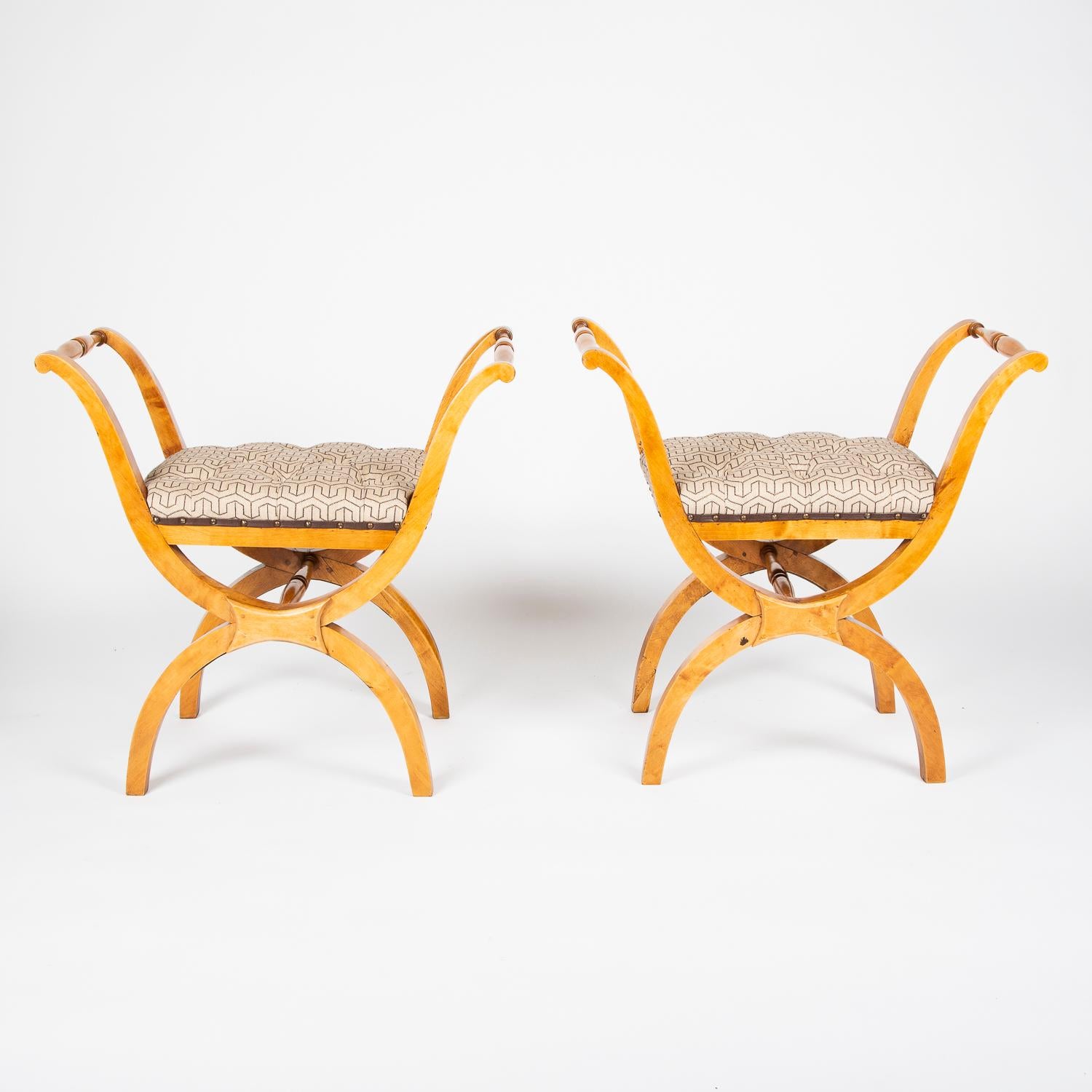 A pair of satin birch X-frame stools or window seats, Swedish, circa 1900.

Seat upholstered in buttoned beige fabric with dark brown geometric design.

 