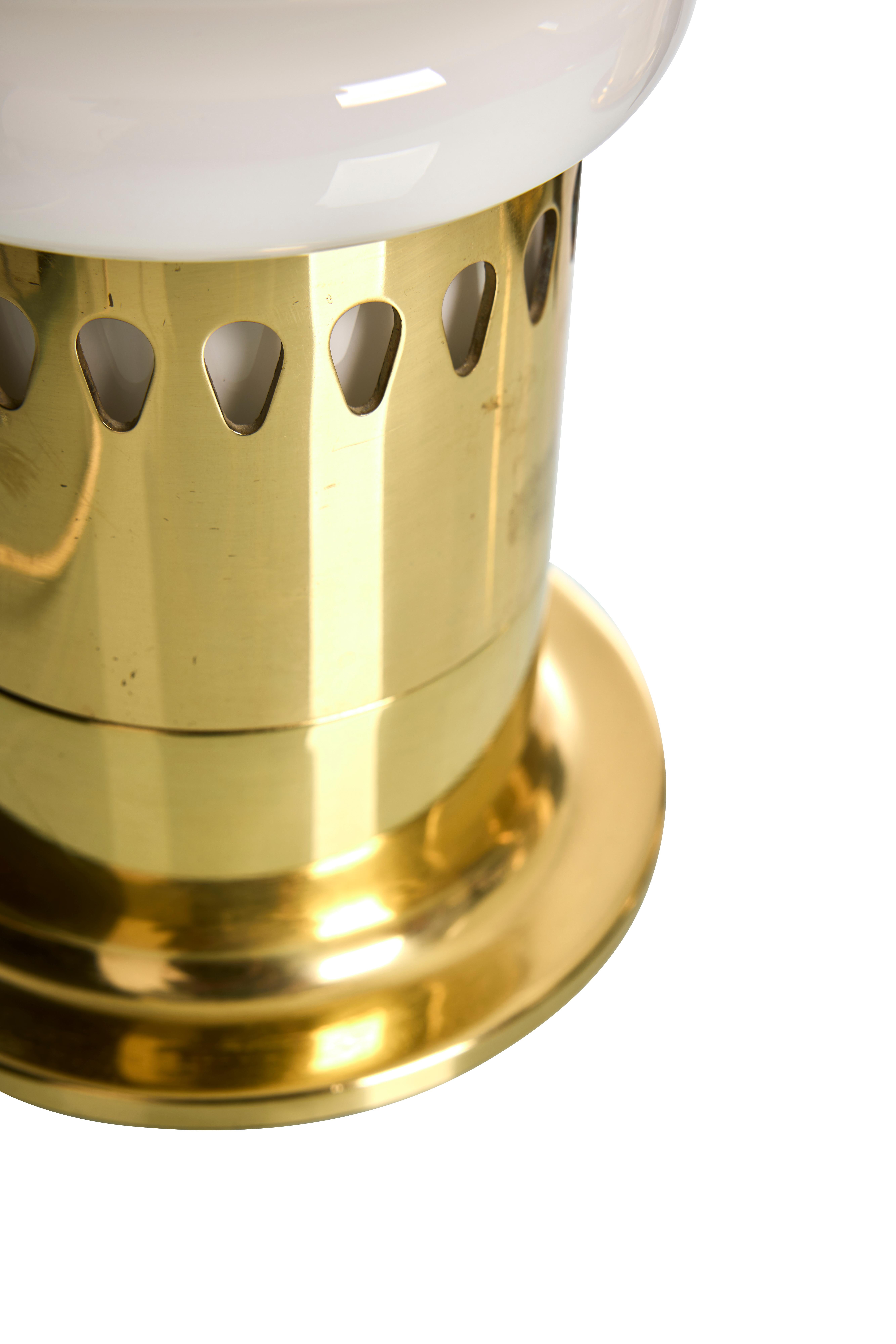 These table lamps, designed by Hans-Agne Jakobsson in the 1960s, feature a combination of brass and glass. The base is made of polished brass with perforated details, supporting an opaline glass shade. The shade has a rounded, smooth surface,