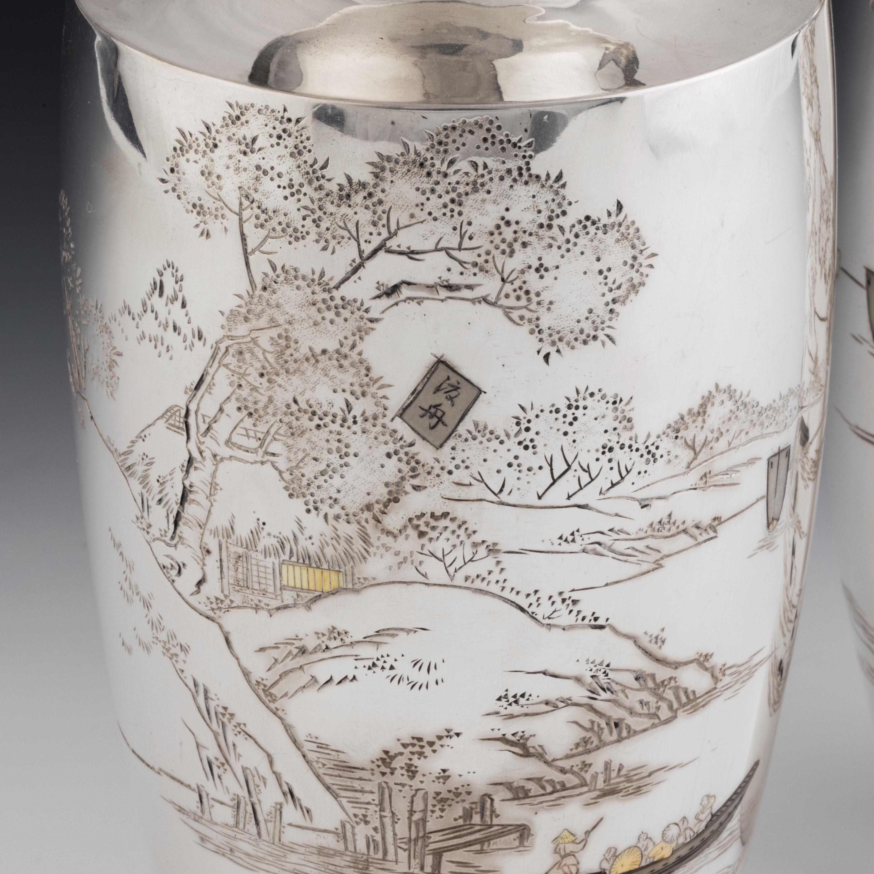 A pair of Taisho period silver vases, each with a waterside scene of sailing boats, punts, ducks and egrets by a jetty in front of flowering trees and hills, with some gilt detailing, signed and assay stamped. Japanese, circa 1920.
 