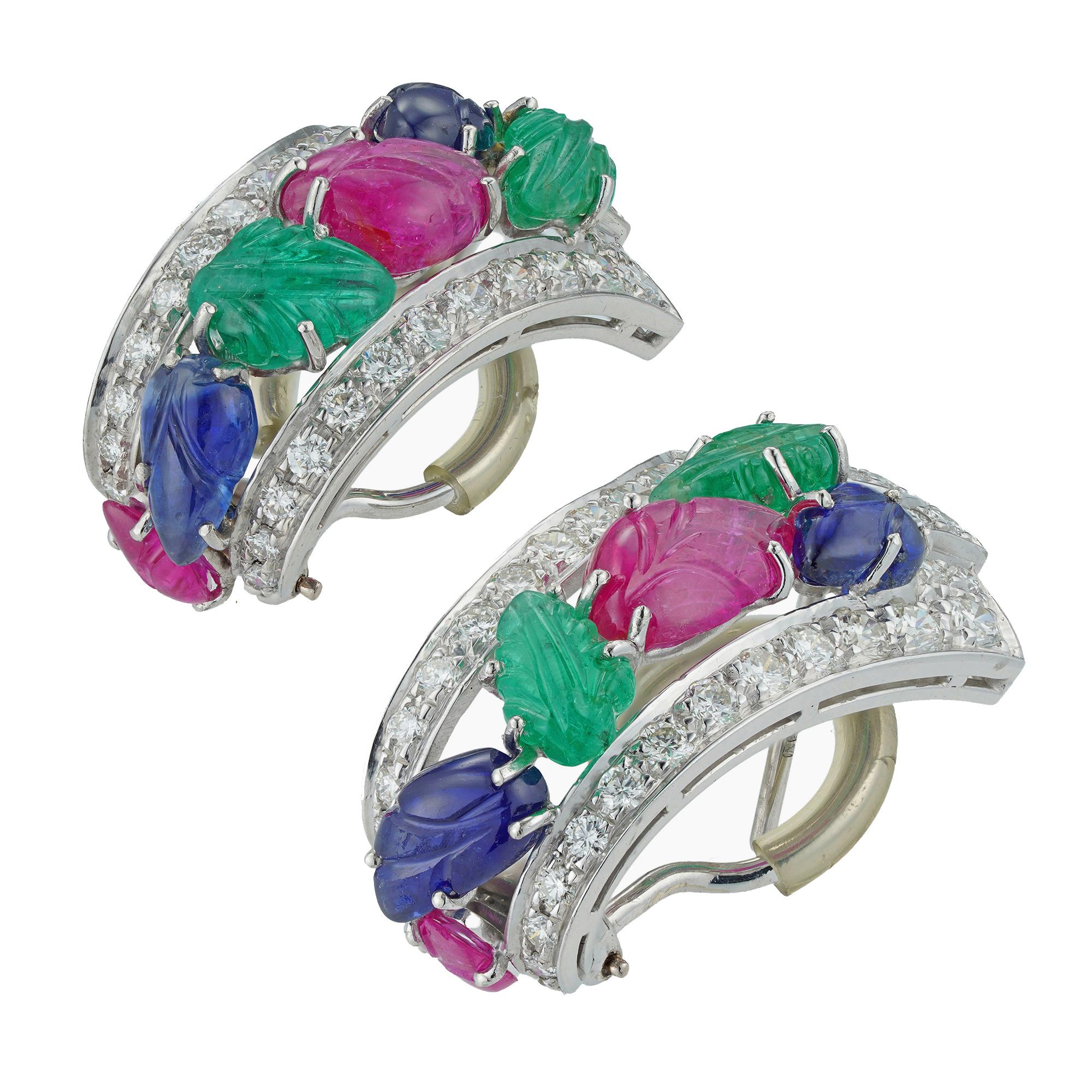 A pair of mid-20th century tutti-frutti clip earrings, each clip with a diamond-set frame of geometric design, grain-set with round brilliant-cut diamonds estimated to weigh 2.5 carats in total, to the centre with two emerald, two sapphire and two