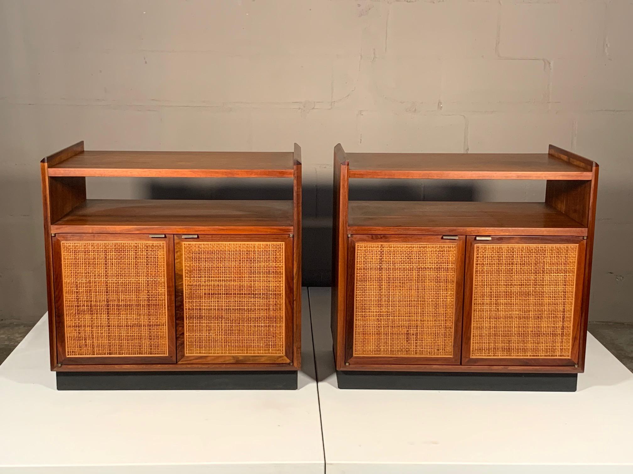 A pair of unusual and multifunctional end tables or nightstands by Jack Cartwright for Founders Furniture. Could also be storage cabinets or small credenzas. Walnut with original caned doors, finished backs and specially designed cutout for storage,
