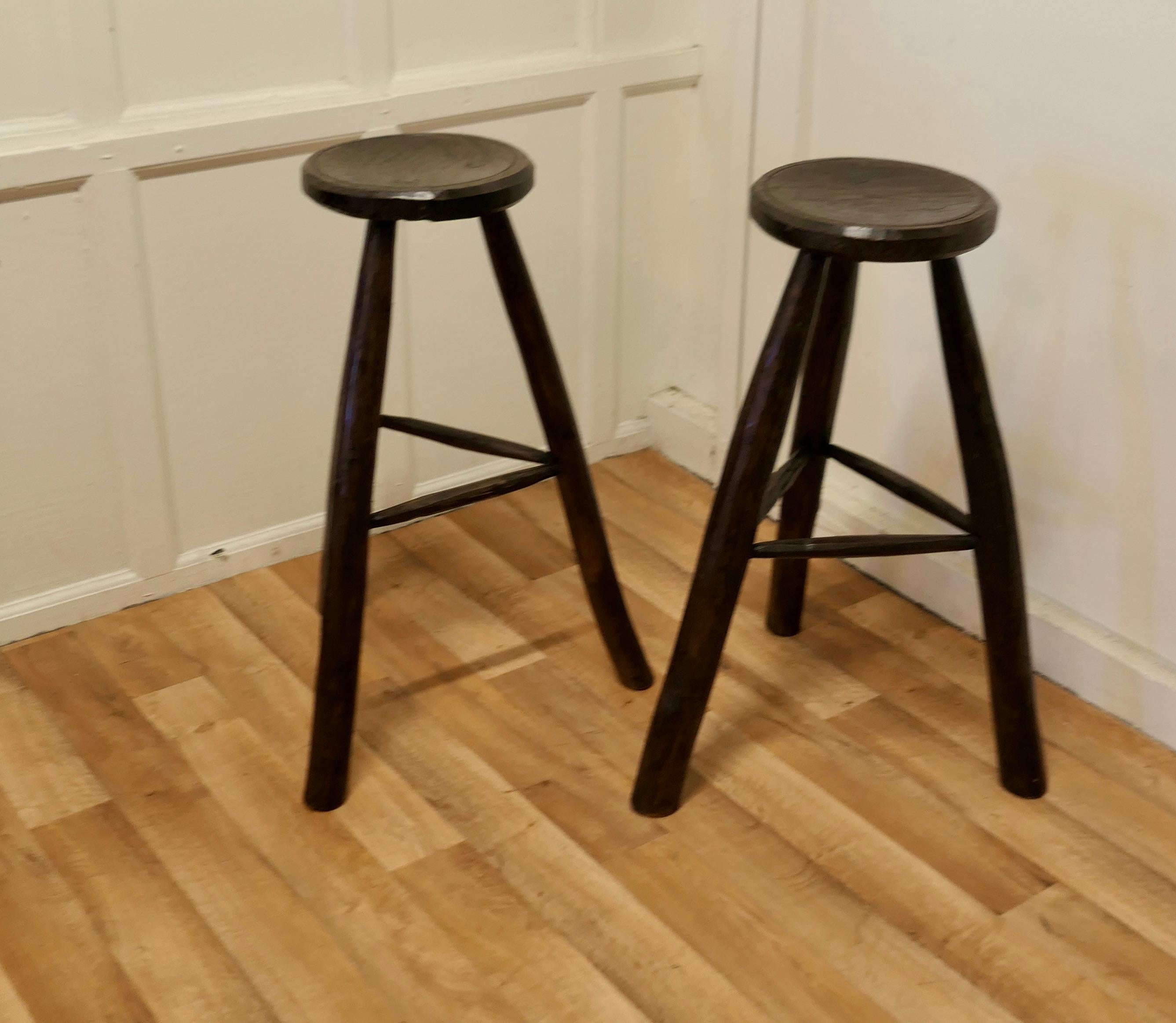 A pair of very rustic 19th century French high stools.

These are long leg stools they are made in ash and elm, the seats are hand carved from one solid piece, each of the 3 legs carved from a single branch and set into the seat.
The Stools are