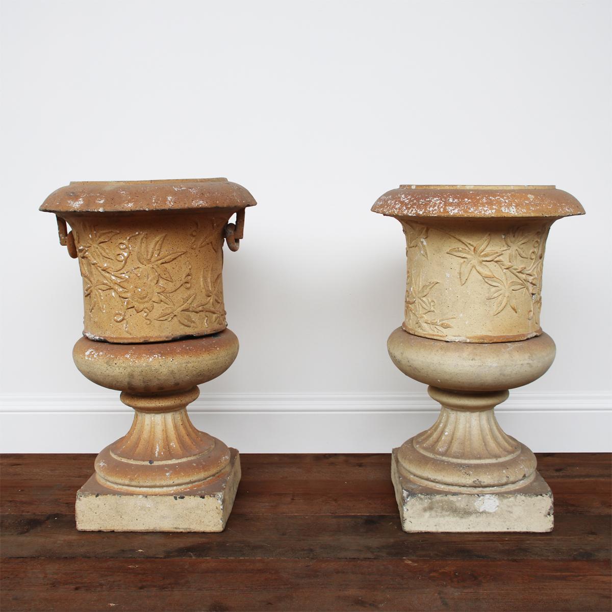 A pair of Victorian clay garden urns on pedestals by the Garnkirk Fireclay Company of Lanarkshire, decorated with a continuous band of passion flowers. One urn is missing its ring handles.

Measures: Overall 48cm diameter x 76cm high. Base 33cm