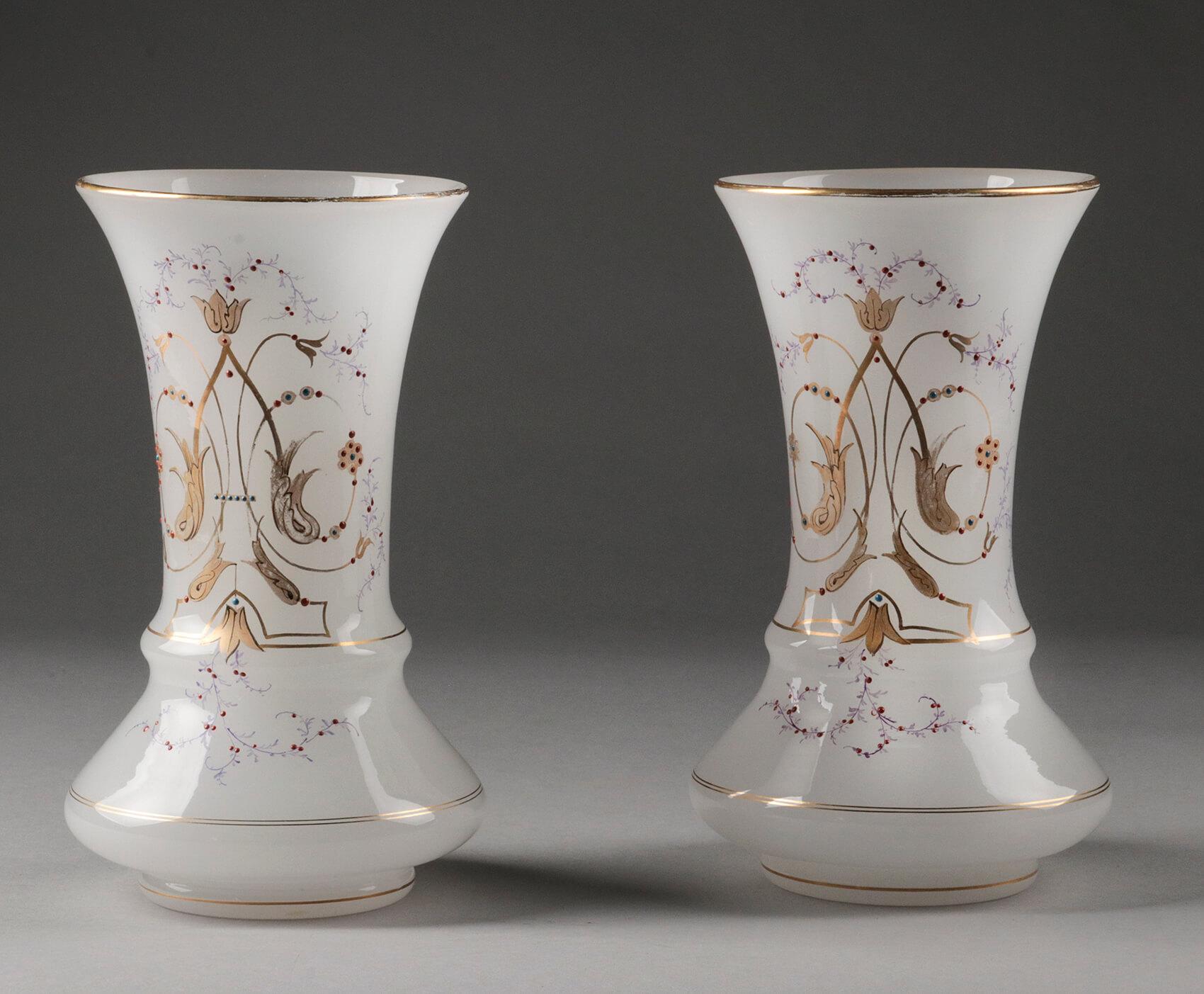 A beautiful pair of antique opaline glass vases from the Victorian era. The vases are hand painted with elegant motifs and gold-colored edges. The decorations stand out beautifully against the white translucent background. The pair of vases comes