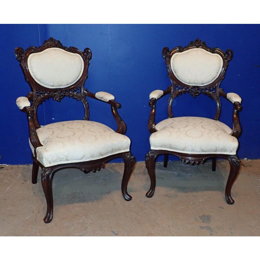A pair of Victorian Rococo Carved Arm Chairs. Pair of ornately carved upholstered arm chairs.