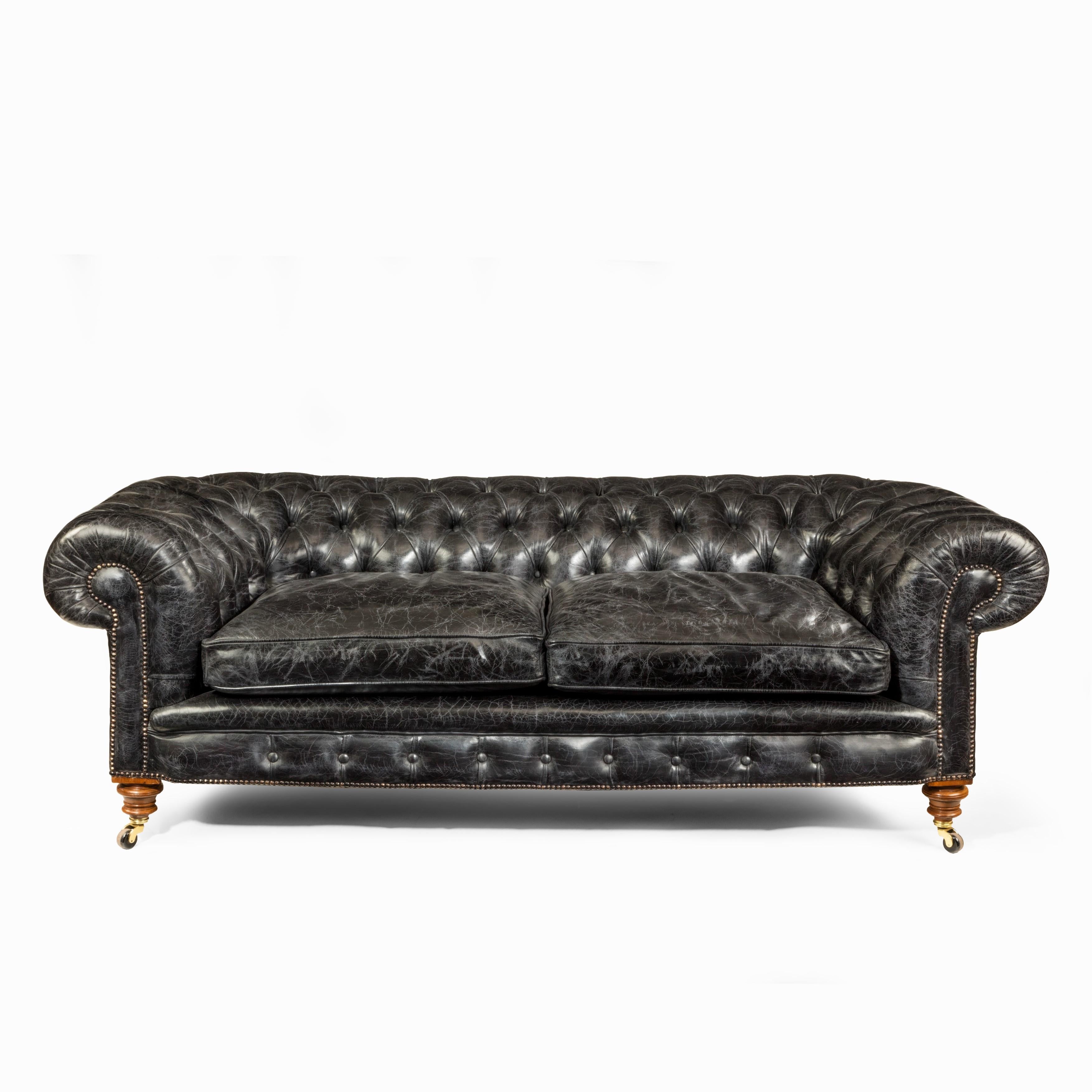 A pair of Victorian three-seat walnut Chesterfield sofas, each of typical form with rolled arms and two-seat cushions, on the original casters, reupholstered in deep-buttoned and distressed black leather, English, circa 1870.
 