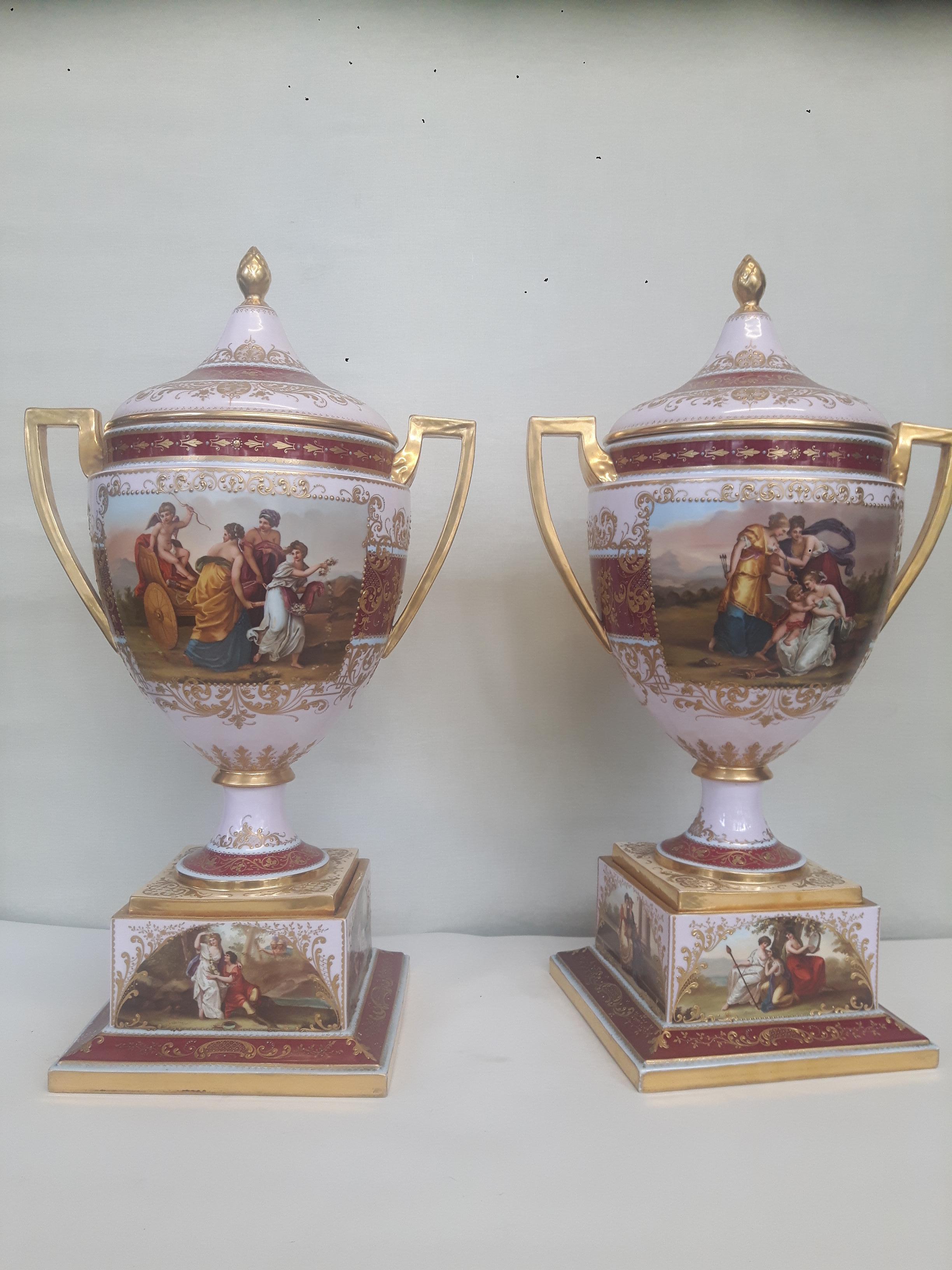 A pair of Vienna style late 19th Century porcelain vases and covers, mounted on plinths of twin handled baluster form, each painted with reserves of classical Gods and Goddesses, against a salmon pink burgundy and turquoise ground, gilt heightened
