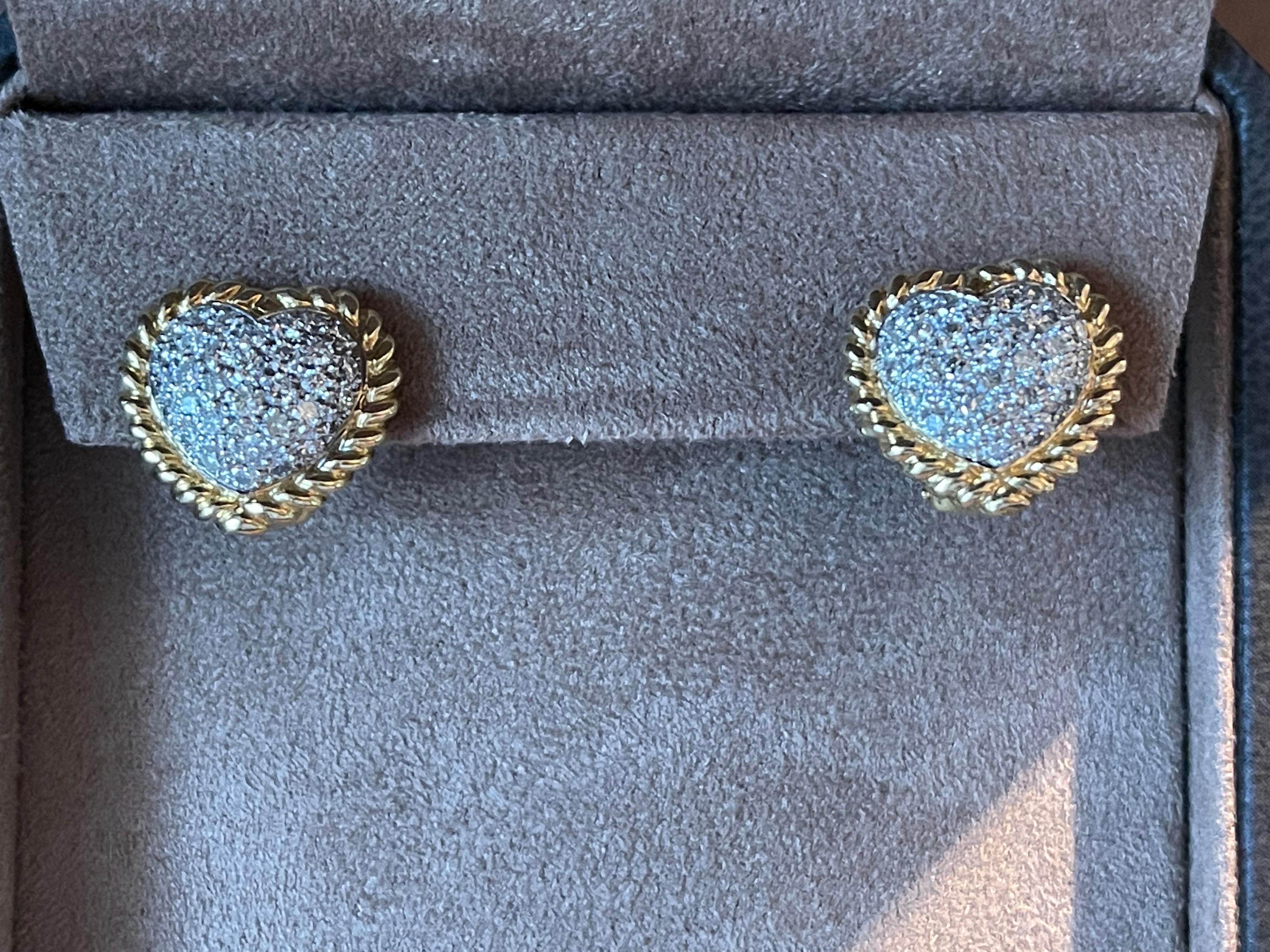 Ein hübsches Paar Diamant-Ohrringe mit Herzmotiv, gefasst in 18 K Gelb- und Weißgold. Sie sind mit einem Pfosten und einer Omega-Klammerbefestigung an der Rückseite befestigt.
Jeder Ohrring zeigt ein Herzmotiv, das wunderschön mit einem gedrehten