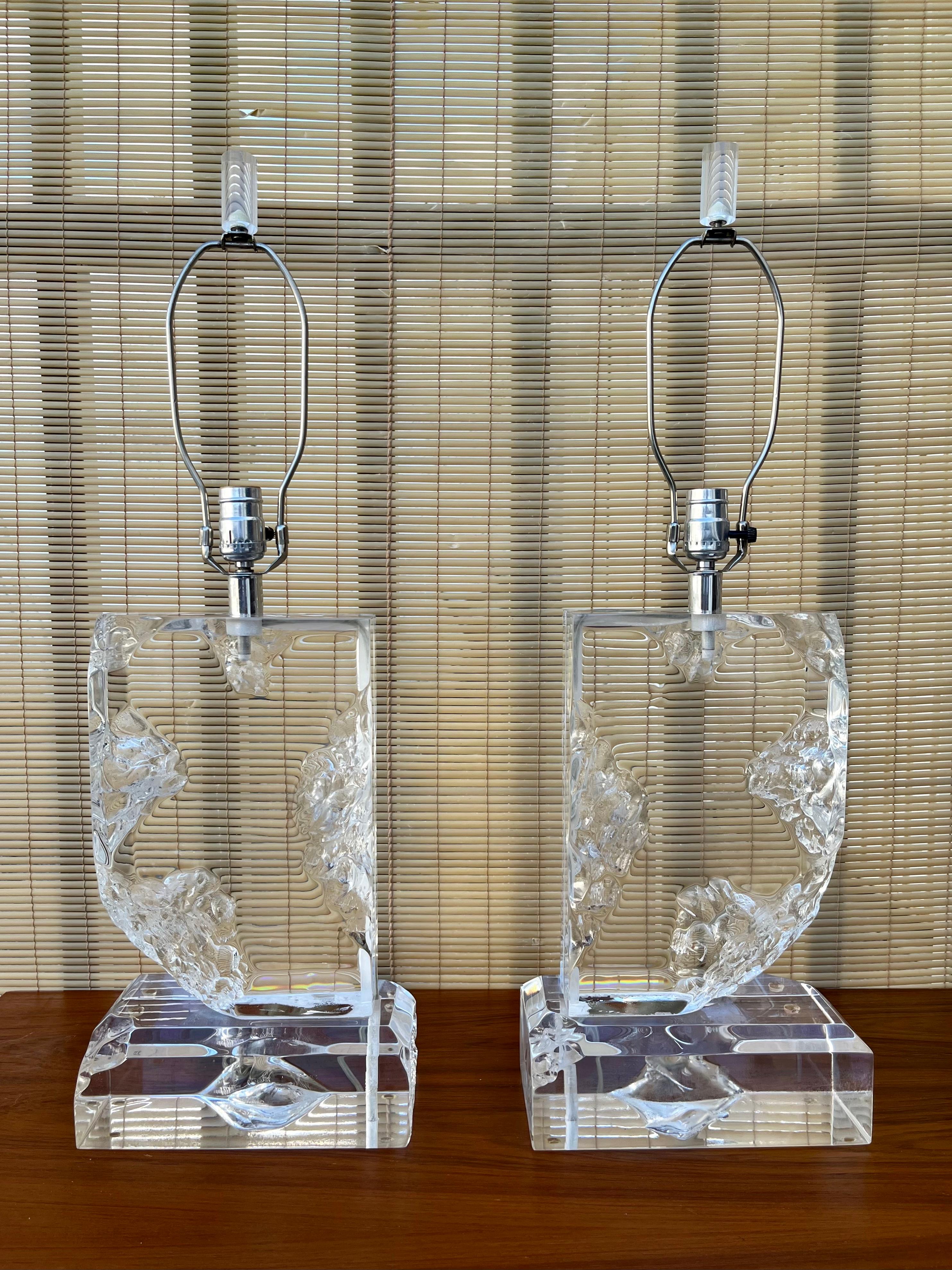 A Pair of Vintage Hollywood Regency Lucite Block Table Lamps. Circa 1970s.s. 
Feature thick sculpted acrylic bases with raw cutout edges resembling ice blocks. With Chromed Hardware and the original lucite finials. 
In Excellent original condition