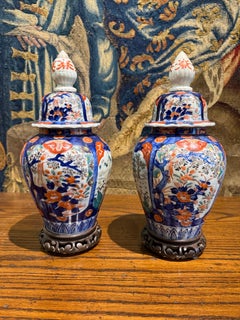 Paire de vases vintage en porcelaine de style Imari, munis d'un couvercle et posés sur des socles en bois