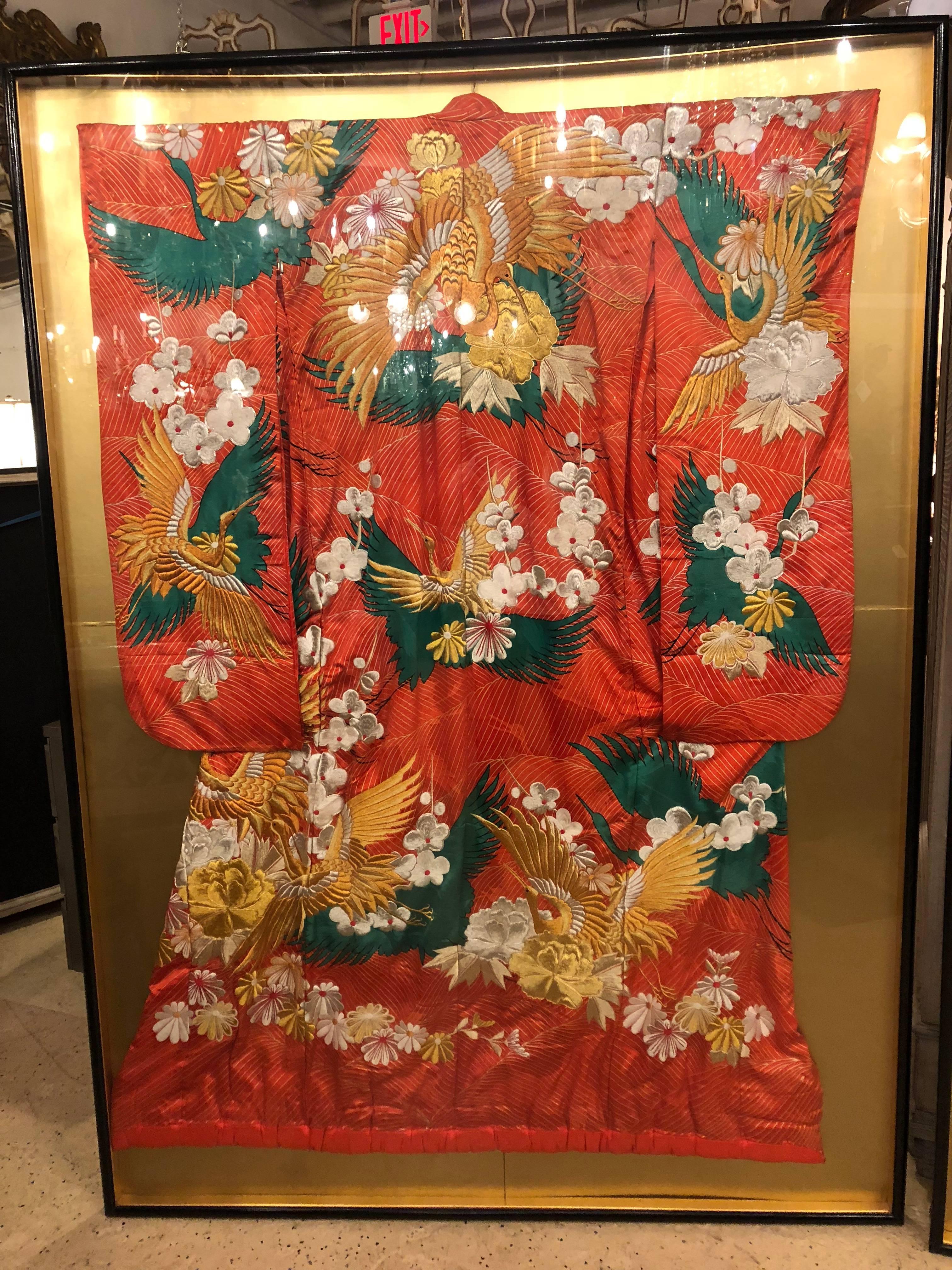 A pair of vintage kimono wedding robes in glass frames. Each finely detailed kimono is embroidered in silk with handwoven with designs depicting birds and flowers. Both sit in a finely ebonized frame under glass.