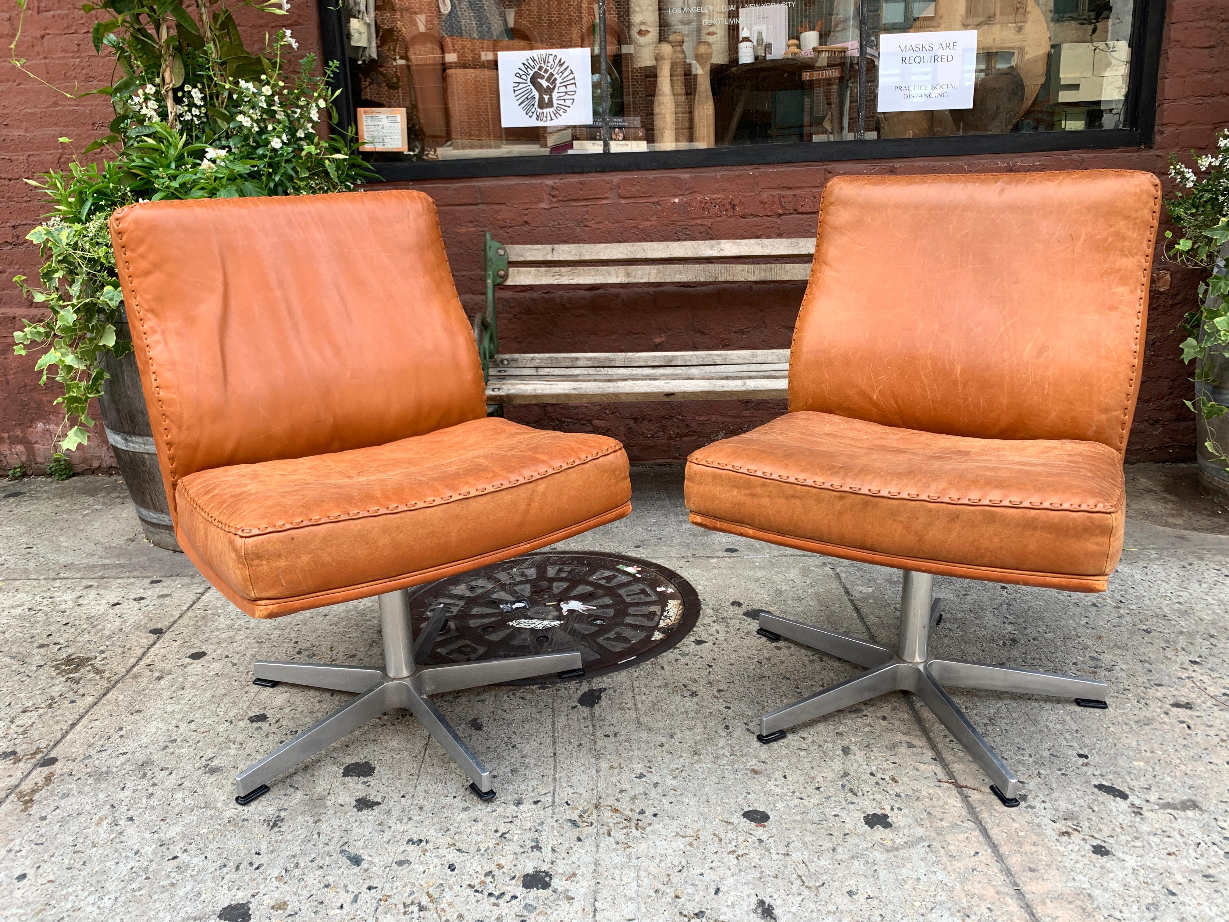 Imagine club chair but in a modern swivel office chair. This duo of vintage leather office chairs is upholstered with a warm and Classic weathered tan color with threaded leather seam.