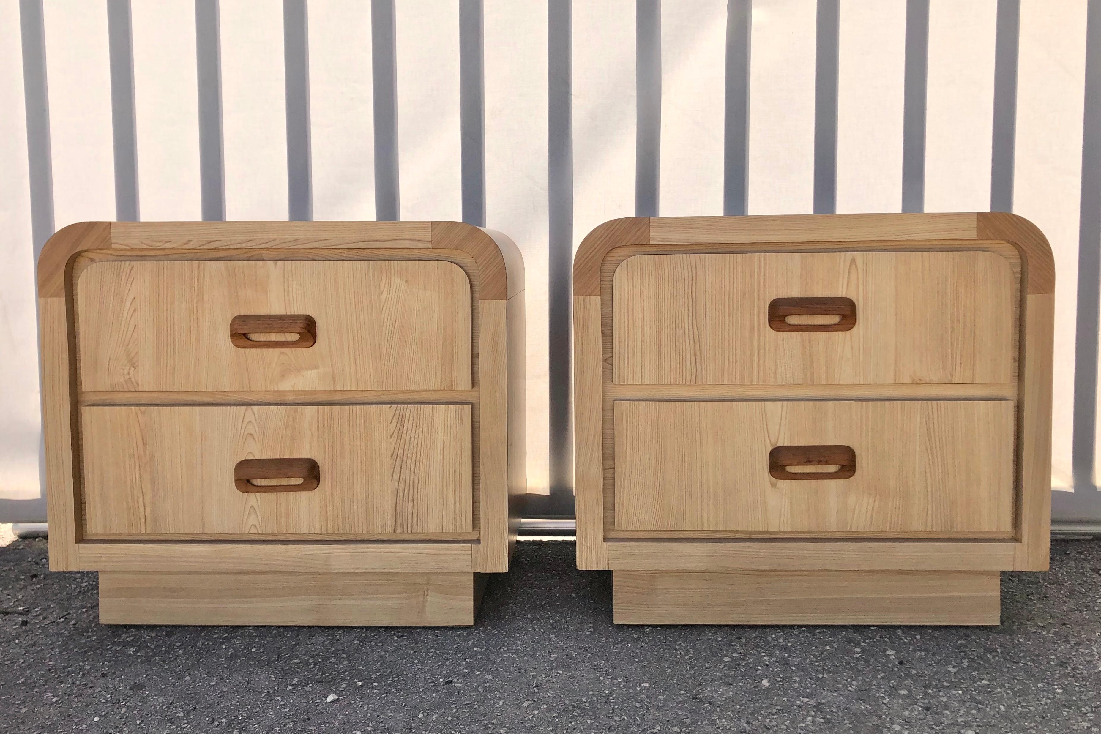 A pair of vintage Post-Modern faux wood laminated waterfall nightstands. circa 1980s. 
Feature two drawers, waterfall sides, a faux light wood laminate finish with darker trims, and solid wood handles.
In good vintage condition with minor signs of