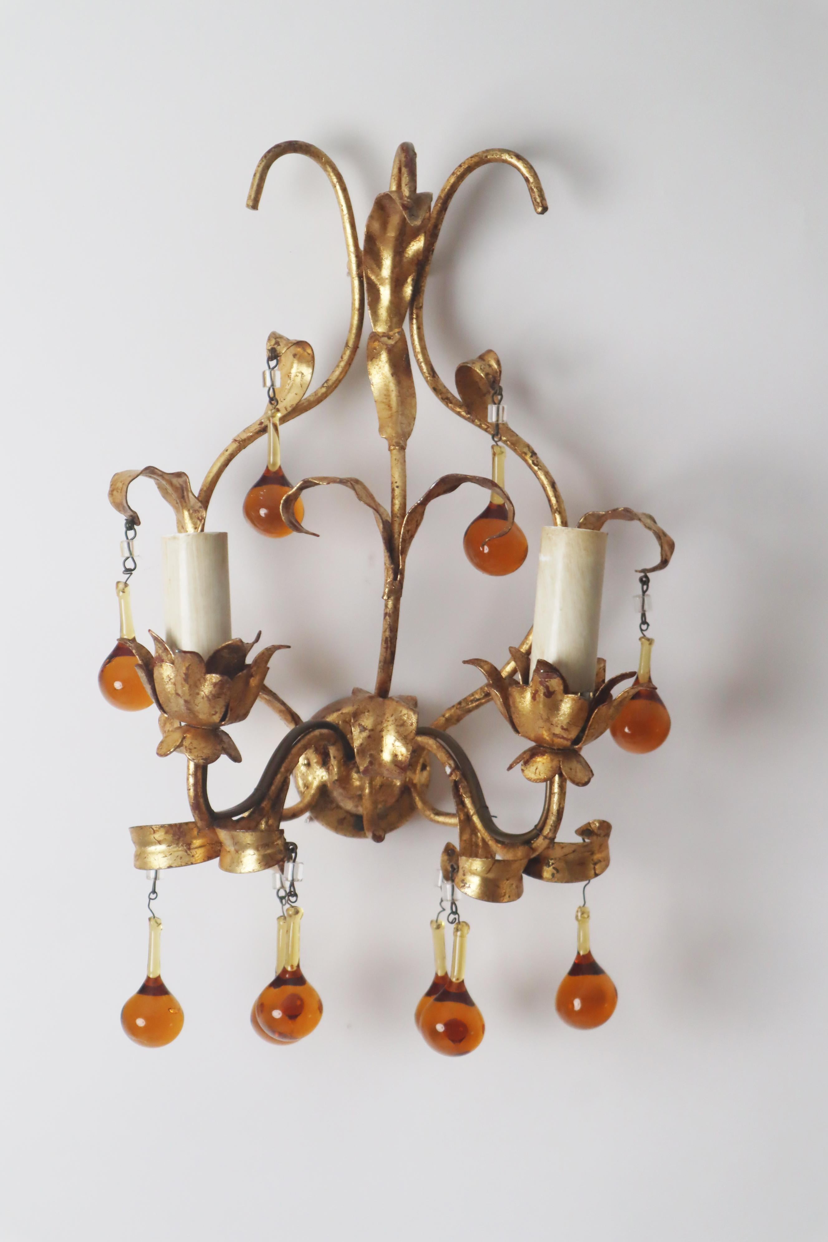 This Vintage florentine pair of wall lamps is made up of glass, metal coated with gold. Each wall lamp has two bulb sockets which makes up a total of four bulbs. each socket bulb has to upto 40 watts. This is a pair of mid-century hollywood regency