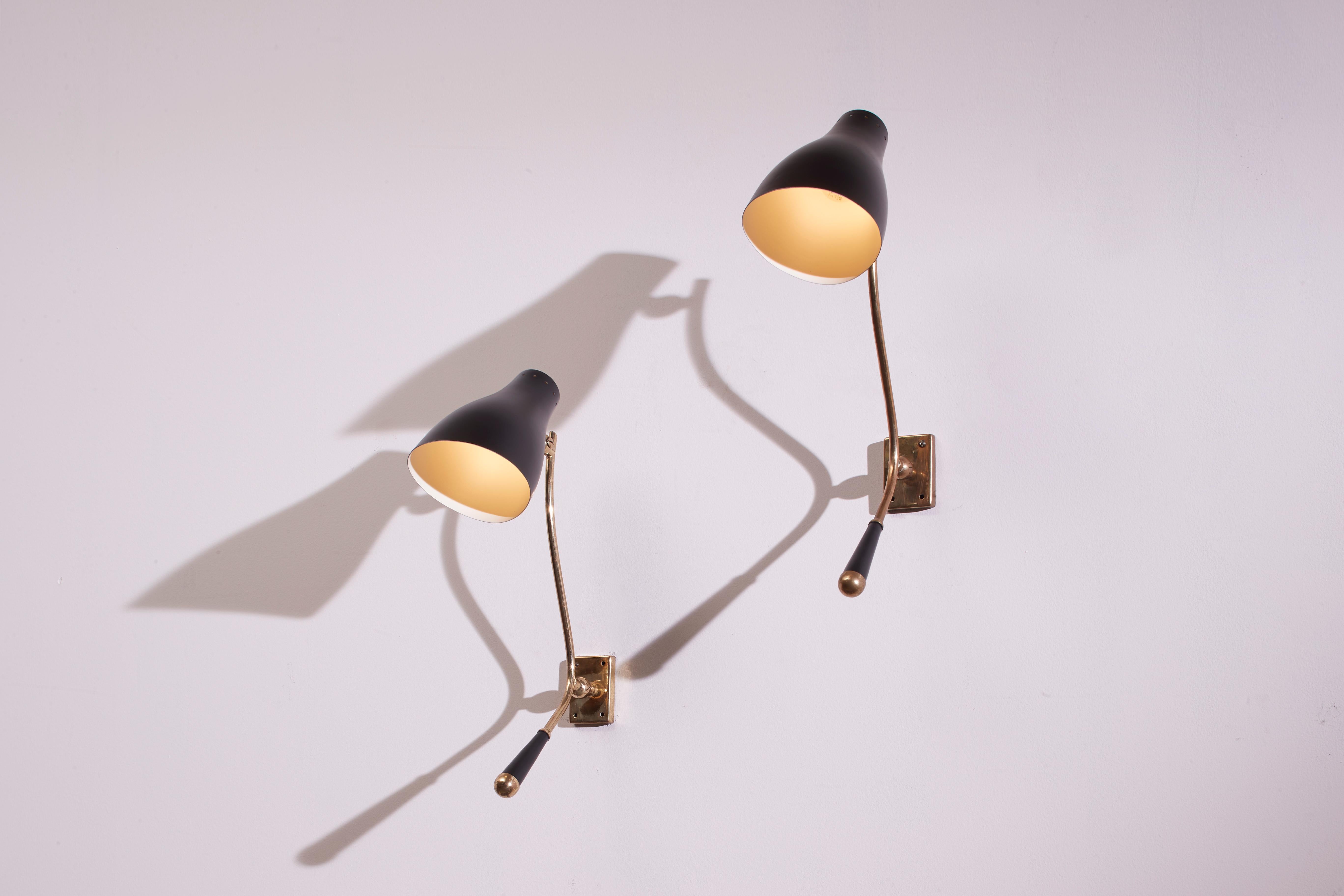 An elegant pair of 1950s wall lamps, made of brass and painted metal, attributed to Stilnovo.

These significant-sized wall sconces stand out for their successful design of the handle, which allows for convenient adjustment of the light direction.