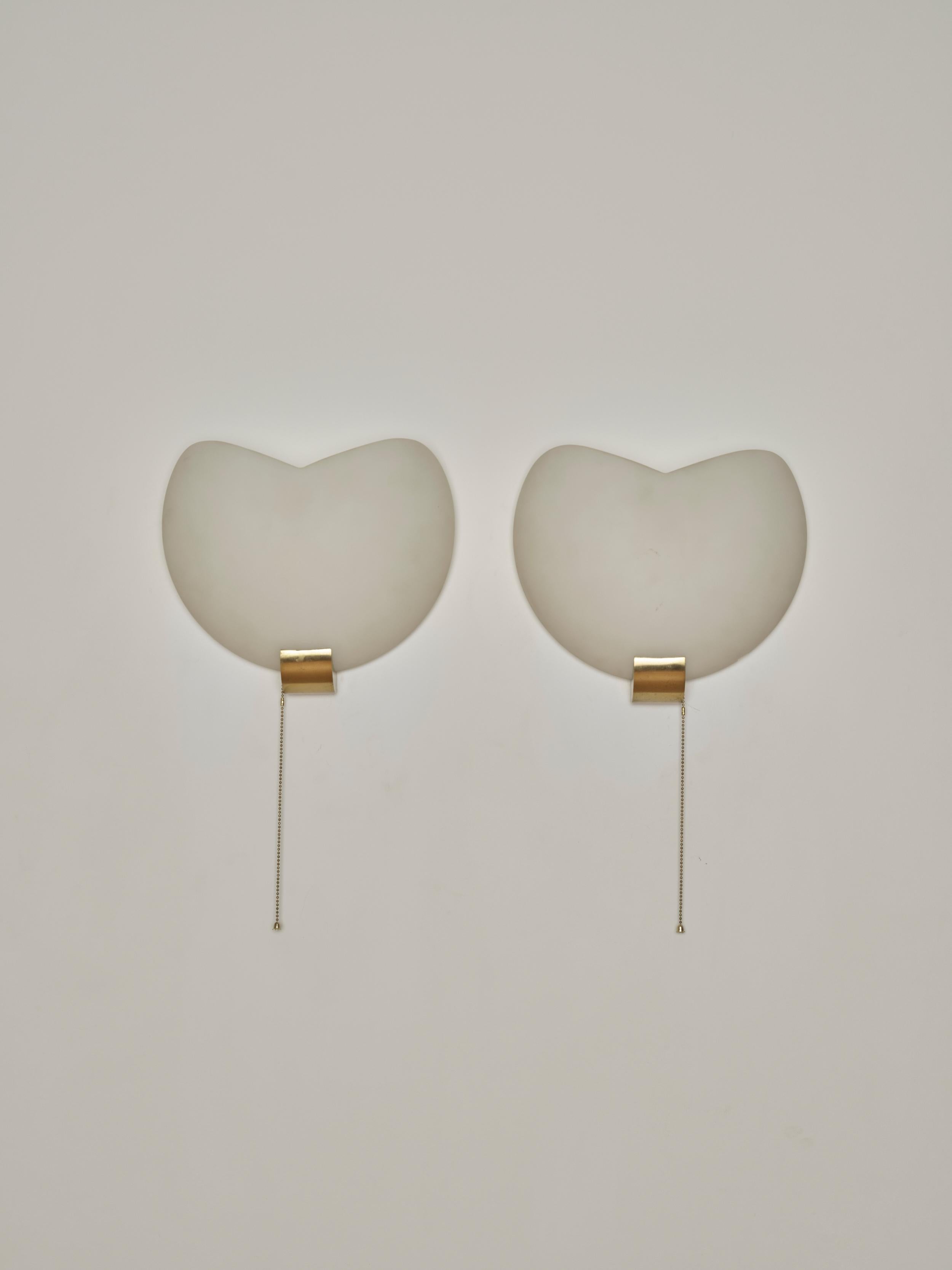 A pair of wall sconces by Jean Perzel in frosted glass with brass and enamel aluminum hardware.

