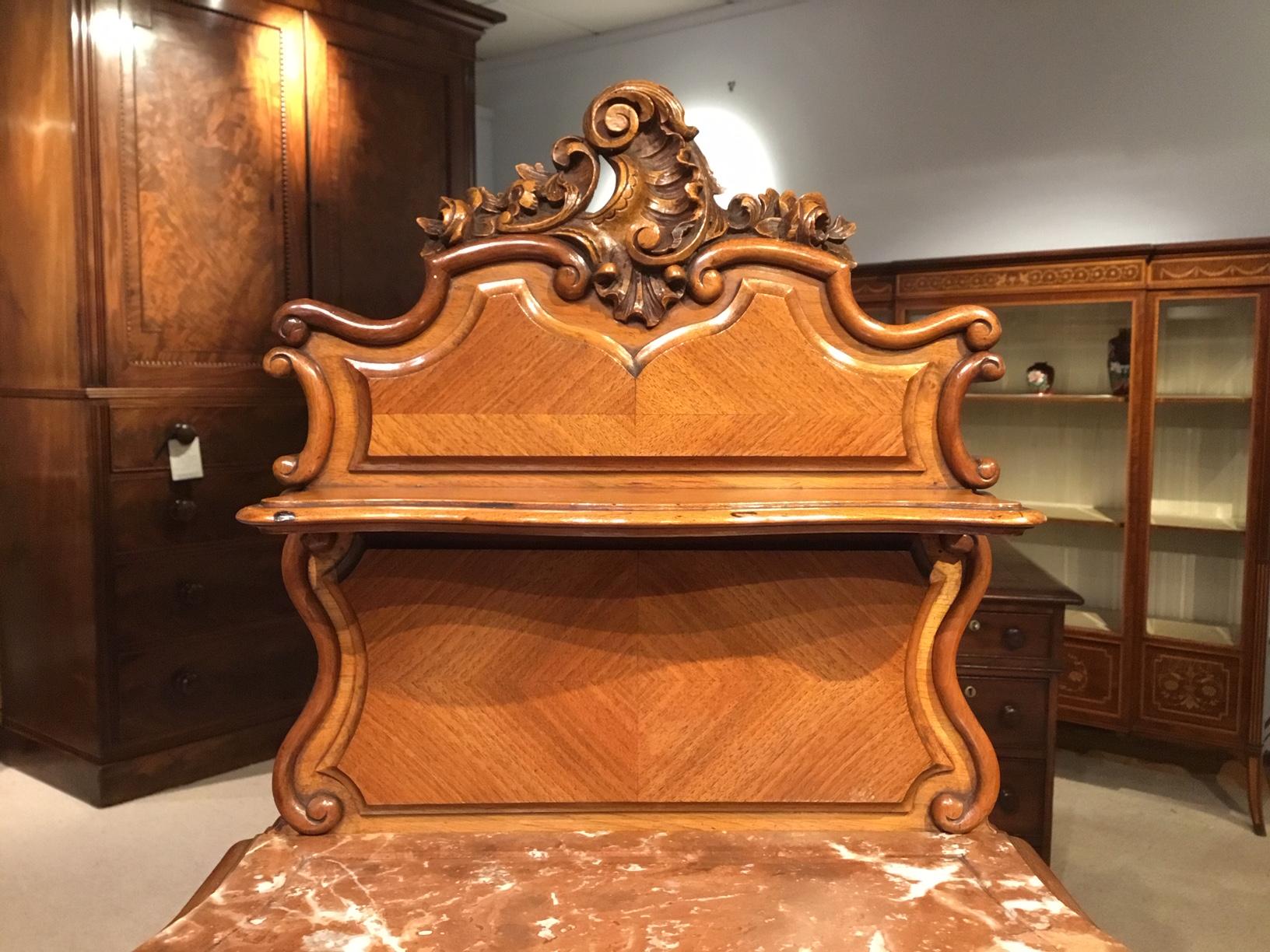 A pair of walnut French late 19th century bedside cabinets. Each with a raised galleried back with a finely carved shell cartouche and a serpentine shaped shelf with further floral detail. Having serpentine shaped rouge marble tops, above a slide,