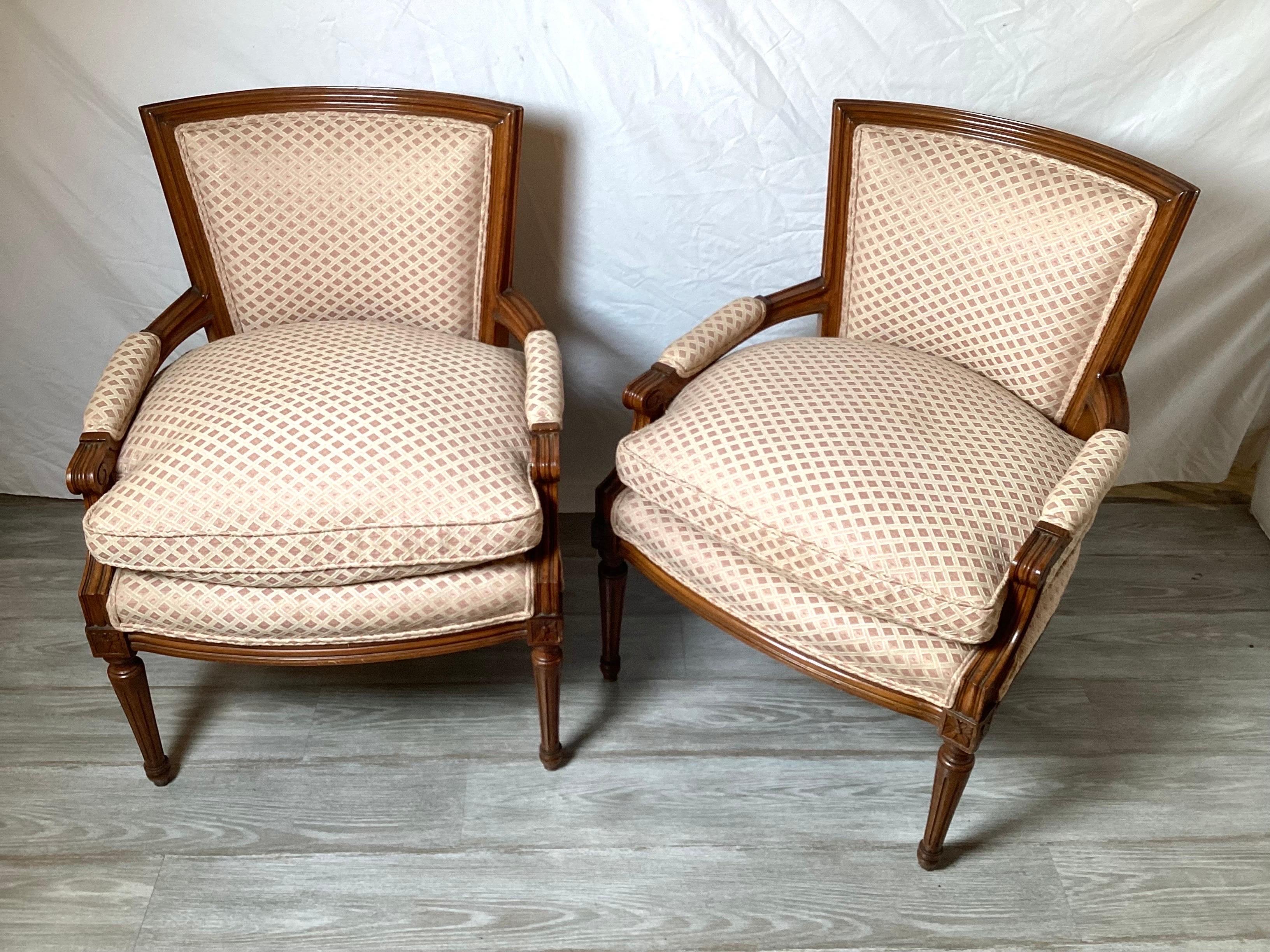 A pair of walnut framed Louis XVI style arm chairs in a blush and cream lattice pattern damask fabric. The overfilled down and feather seats with squared backs and tapering legs.
