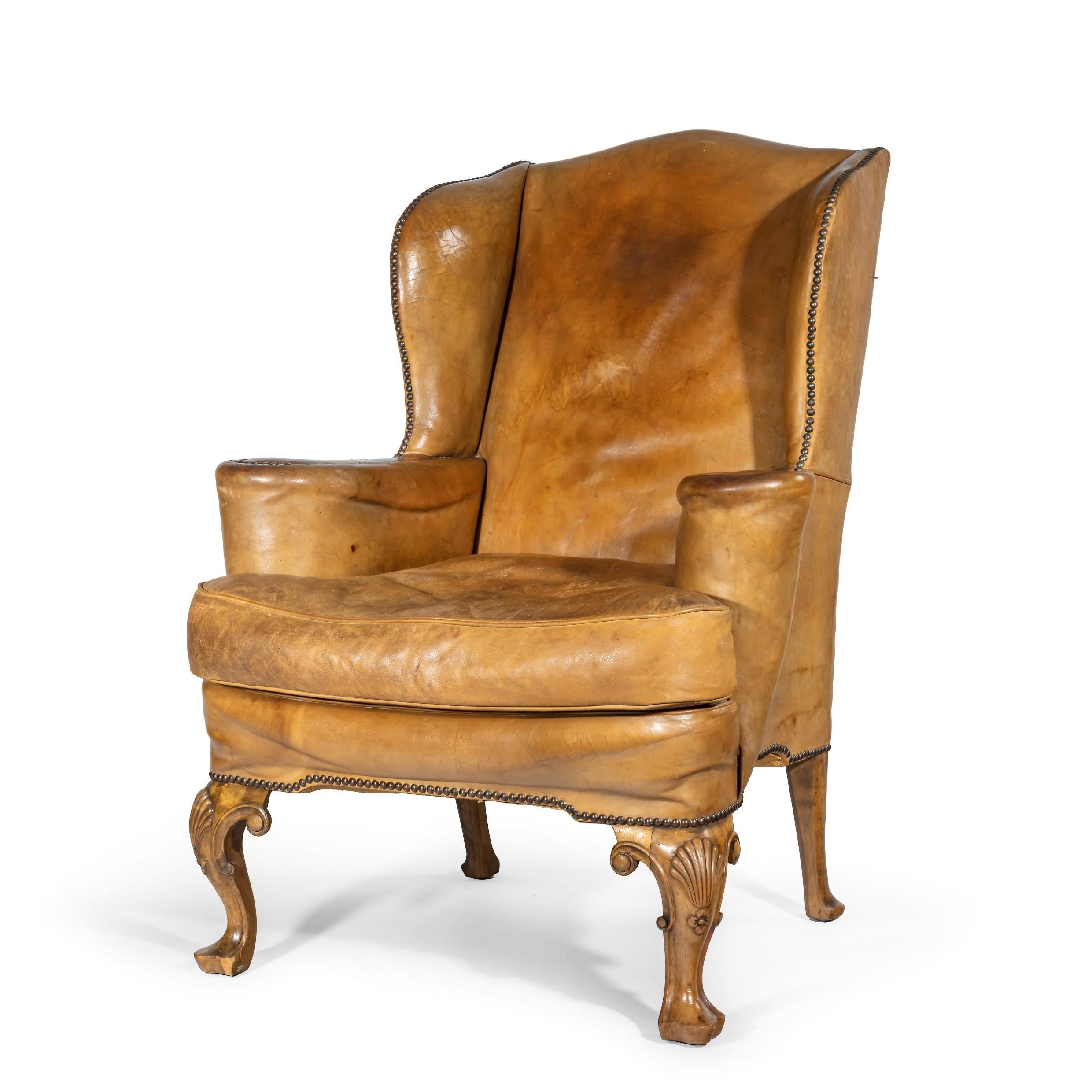 A pair of walnut wing armchairs in the Queen Anne style, the front legs carved with shells on the knees. English, circa 1920.

 